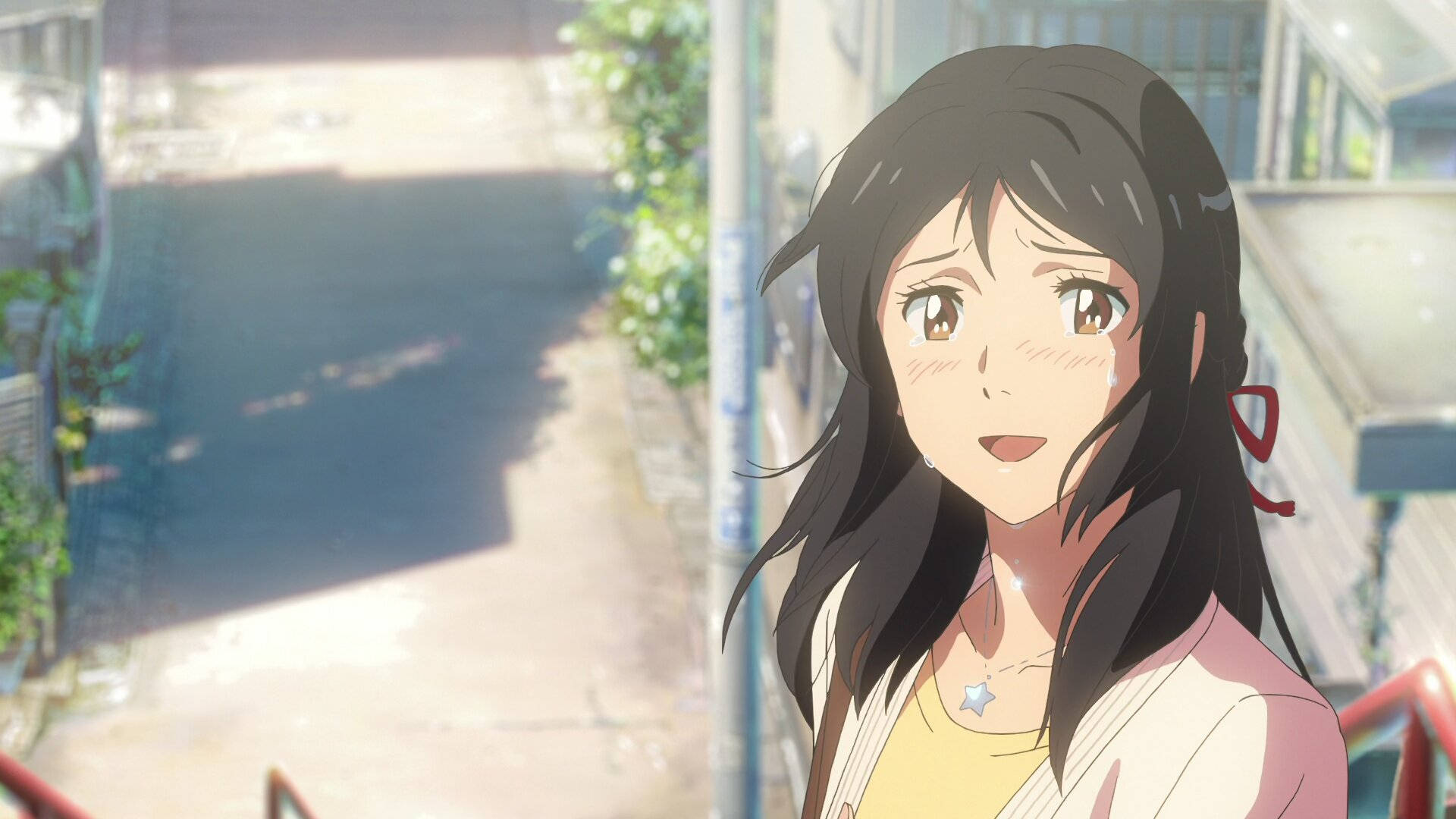 Makoto Shinkai 桌布 壁紙 — 一位開朗的動漫女孩，長著深色長髮，戴著星星項鍊，在陽光明媚的城市街道上溫暖地微笑。