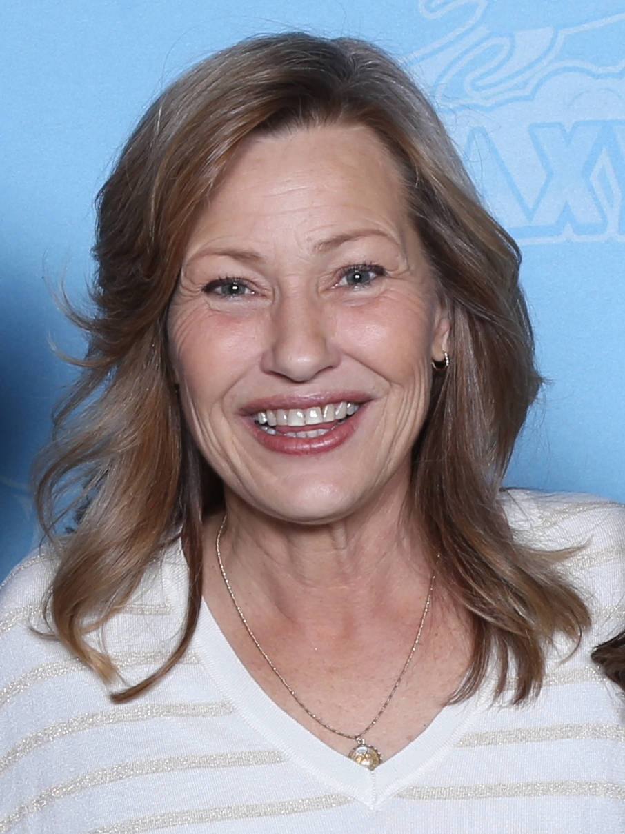 Celebrity 桌布 壁紙 — 一位開朗的女性，波浪形棕色頭髮，在純藍色背景前穿著白色條紋毛衣，溫暖地微笑。