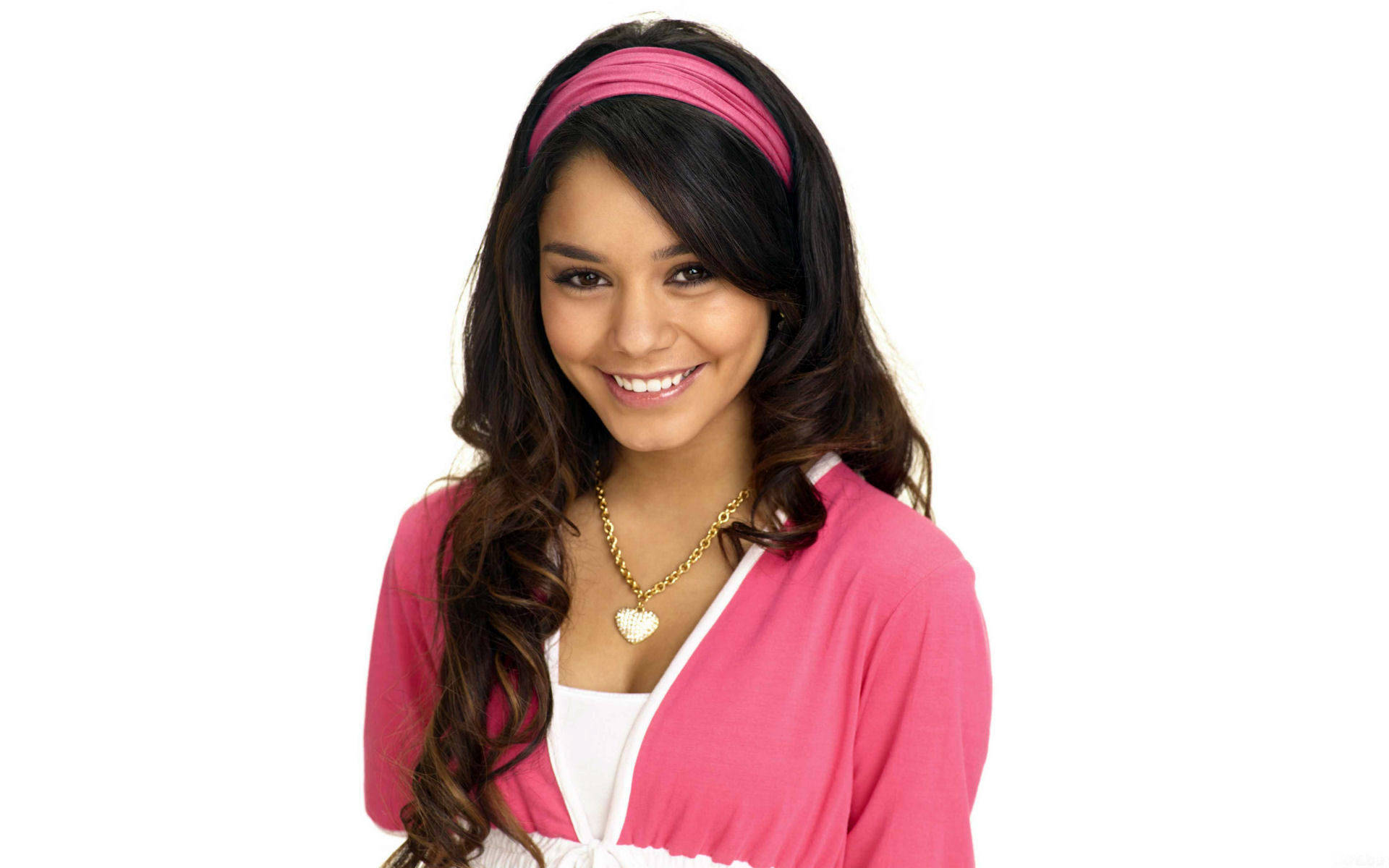 Vanessa Hudgens 桌布 壁紙 — 一位開朗的年輕女性，長長的黑髮，戴著粉紅色頭帶和相配的開襟衫，在純白色背景前溫暖地微笑。