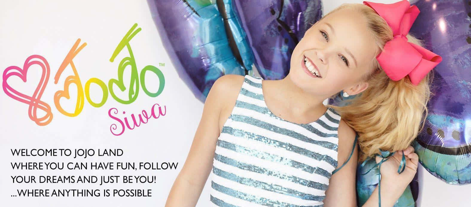 JoJo Siwa 桌布 壁紙 — 一位開朗的金髮年輕女孩戴著粉紅色蝴蝶結，在色彩繽紛的Jojo Siwa標誌旁微笑著拿著閃亮氣球。