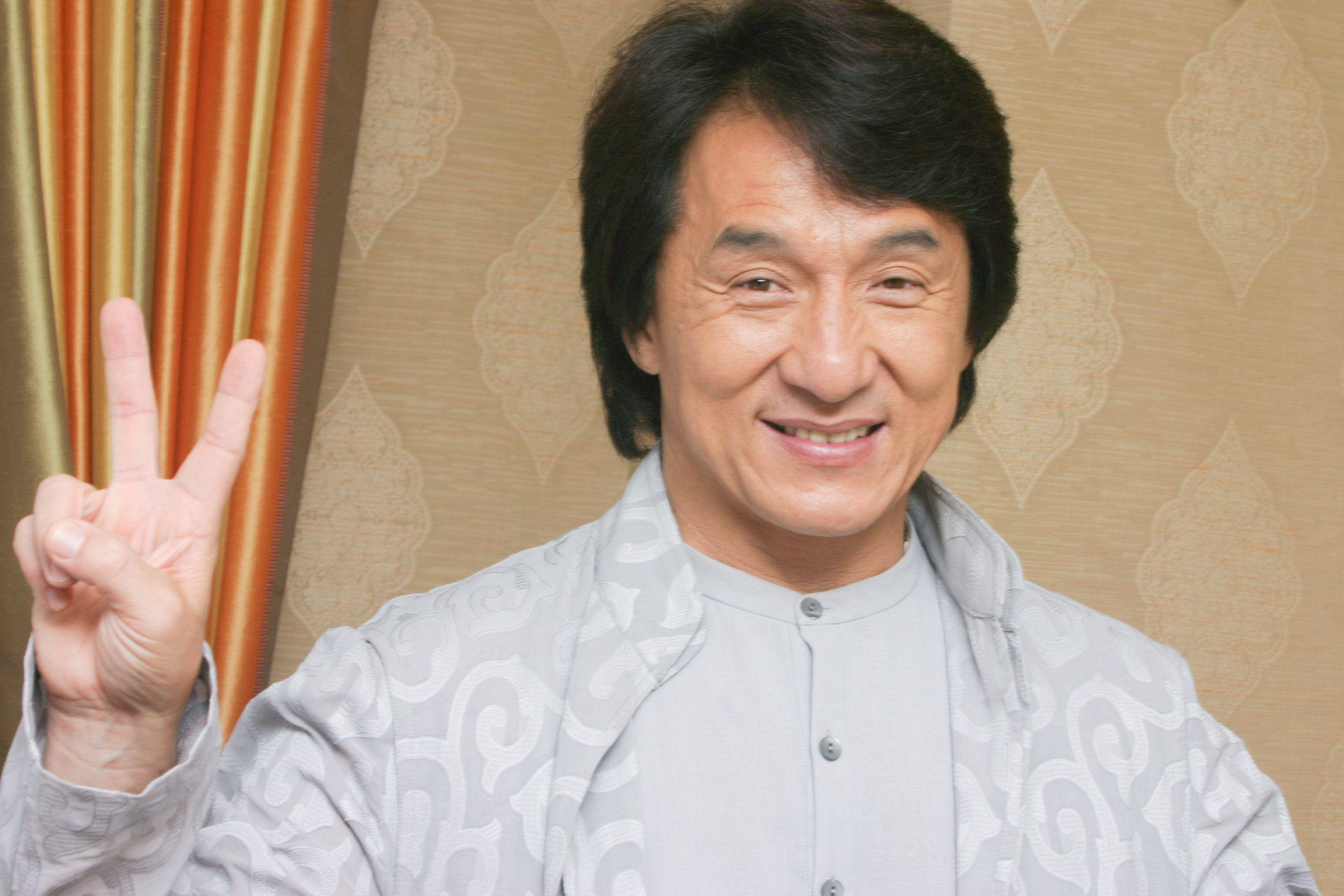 橘色 桌布 壁紙 — 一位開朗的黑髮男子在圖案壁紙和條紋窗簾前微笑著做出和平手勢。