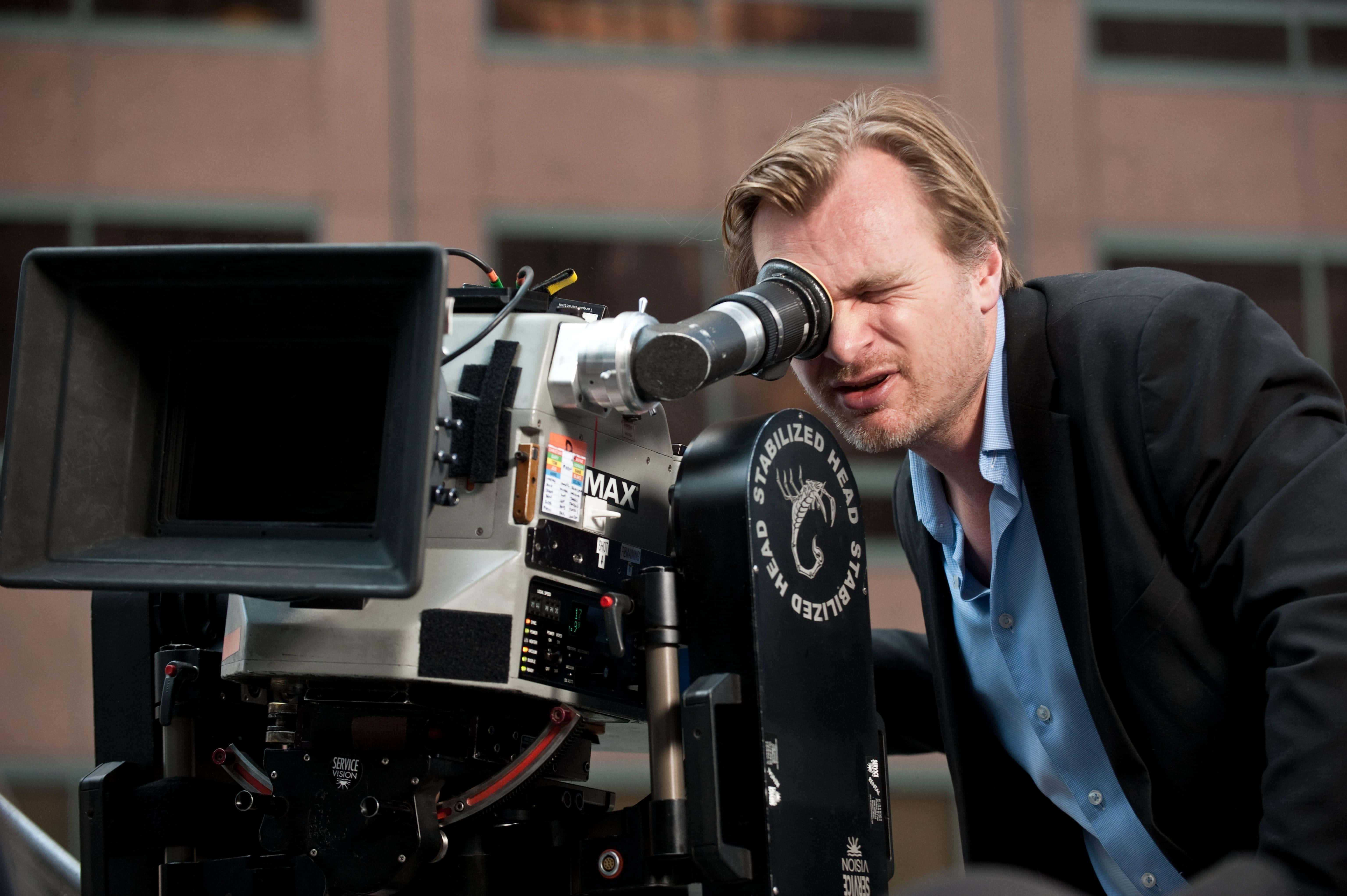 Christopher Nolan 桌布 壁紙 — 一位電影製作人在白天透過城市屋頂上的大型專業電影攝影機專注地凝視。