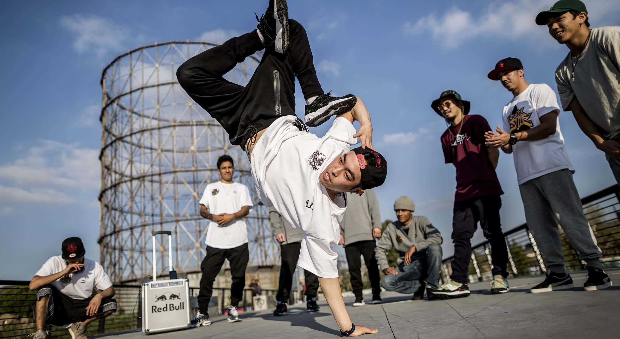 hiphop 桌布 壁紙 — 一位霹靂舞者在屋頂上表演倒立，朋友們在煤氣罐附近的晴朗藍天下觀看。