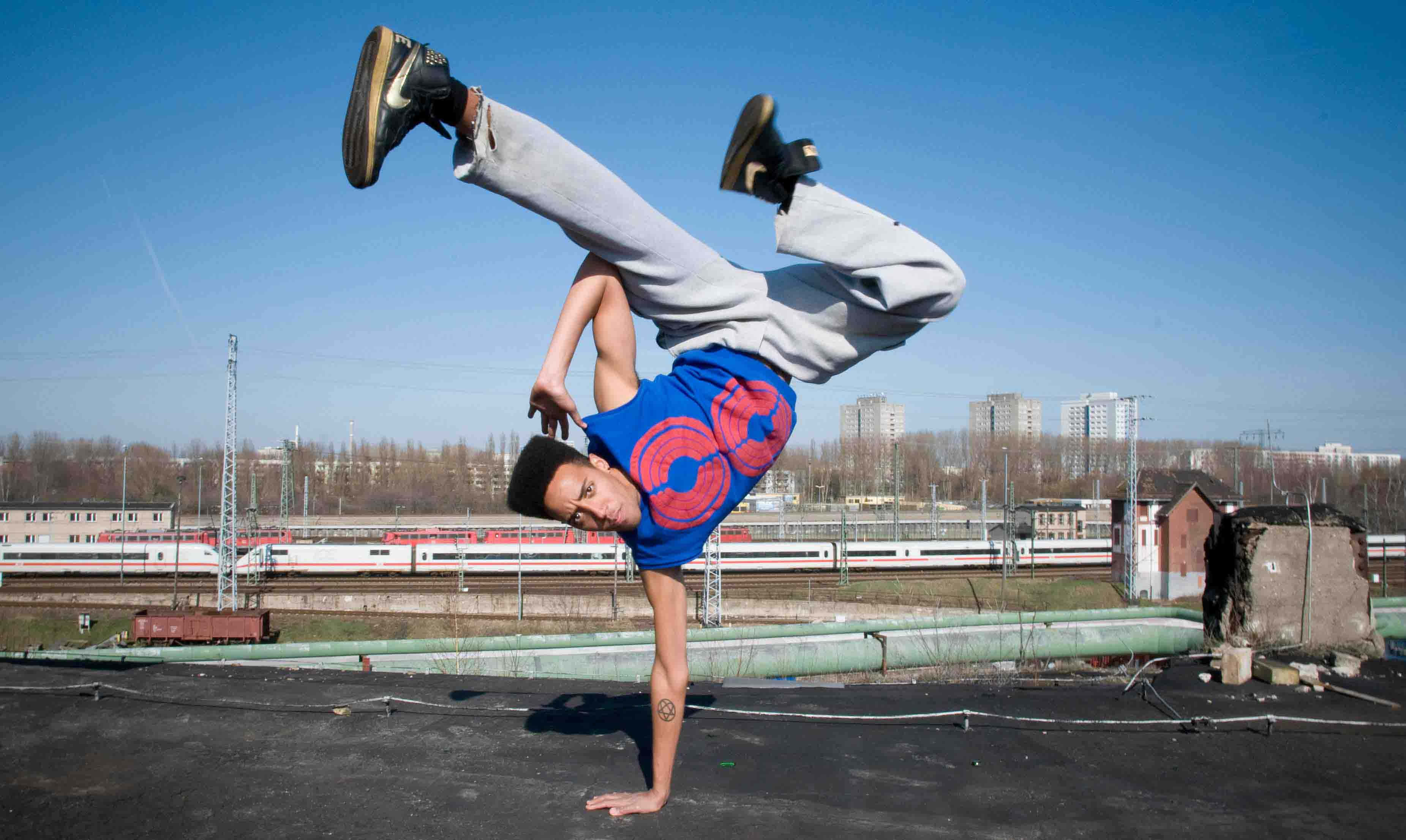 hiphop 桌布 壁紙 — 一位霹靂舞者在屋頂上表演倒立，火車在晴朗的藍天下駛過。