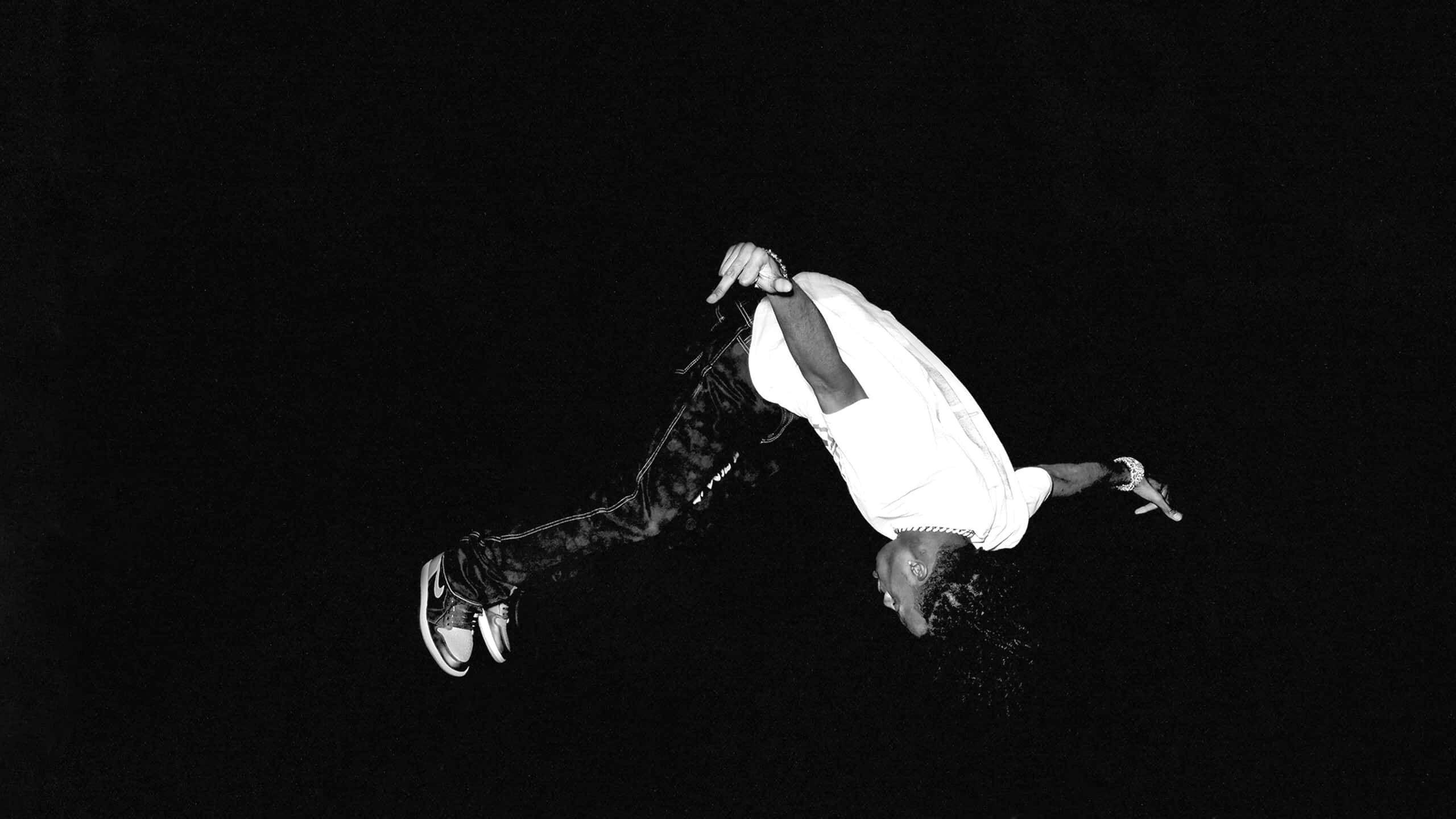 Playboi Carti HD 桌布 壁紙 — 一位霹靂舞者在空中做出戲劇性的倒立姿勢，背景為單色調的純黑色。