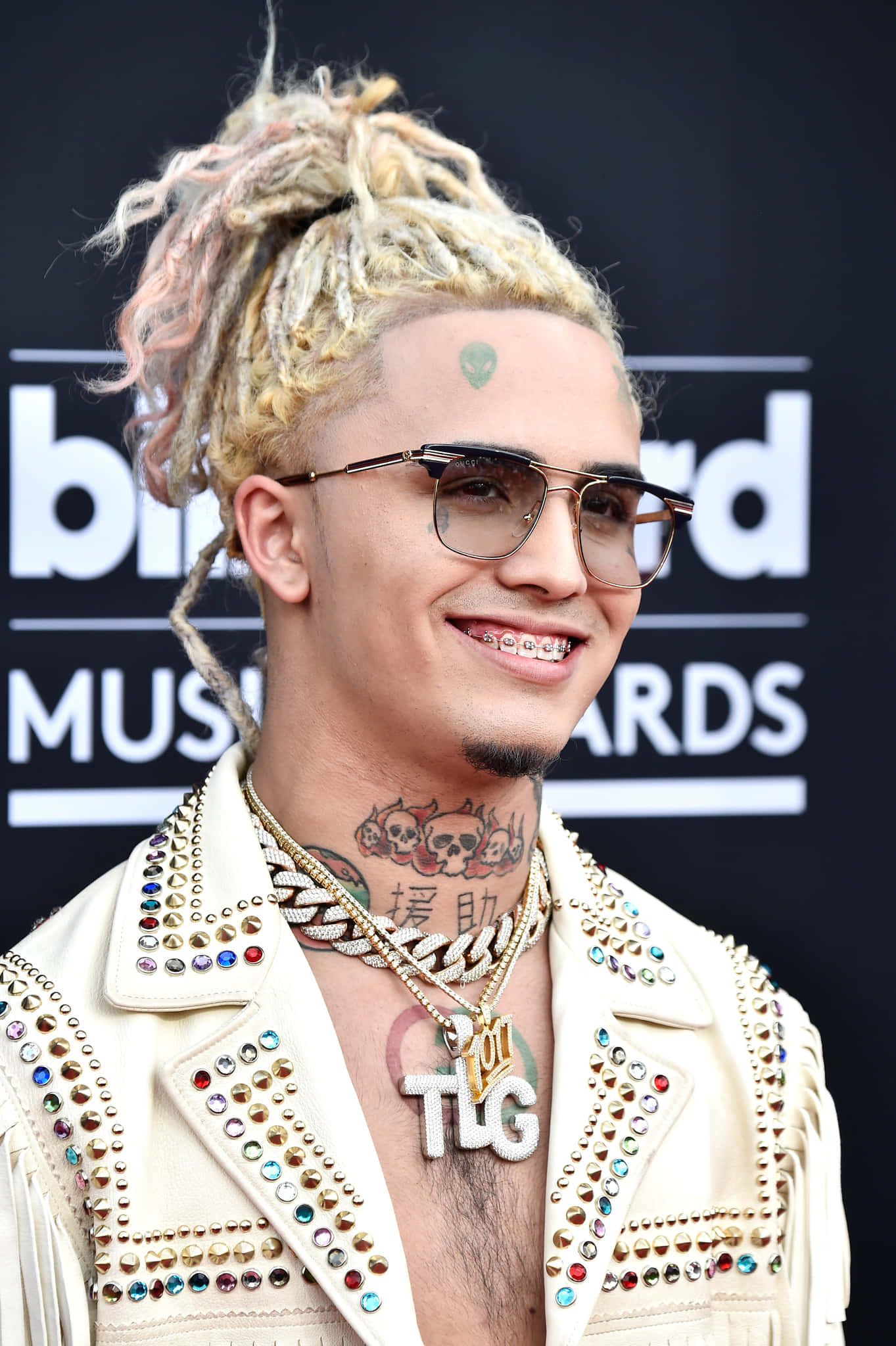 桌布 壁紙 — 一位面帶微笑、擁有彩色辮子頭和眼鏡的男子，在Billboard音樂獎上穿著飾有鉚釘的奶油色外套。