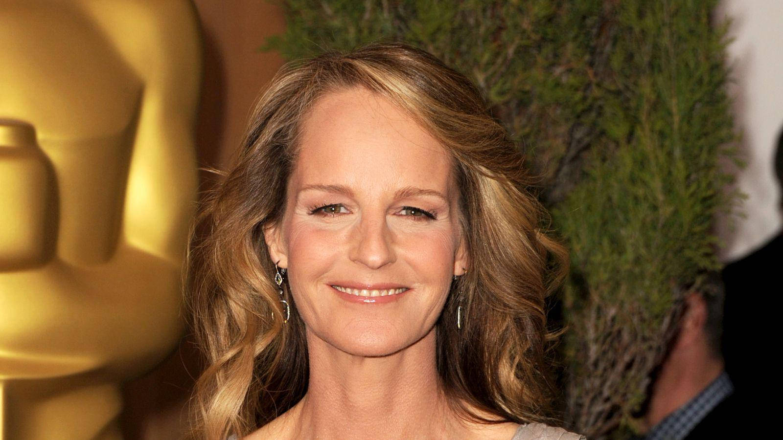 Celebrity 桌布 壁紙 — 一位面帶微笑、擁有波浪金髮的女性站在金色奧斯卡獎座和綠色樹葉前。