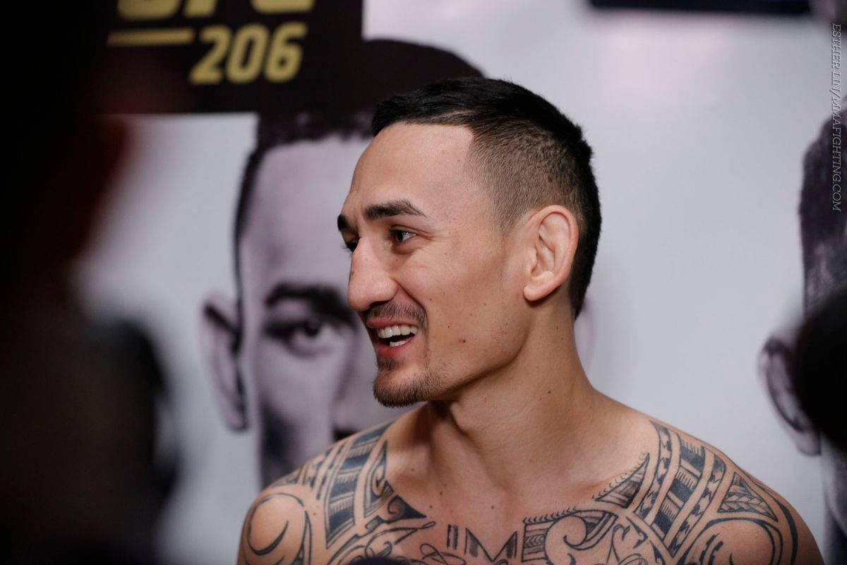 UFC 桌布 壁紙 — 一位面帶微笑、有刺青、短黑髮的戰士站在模糊的UFC 206背景前。