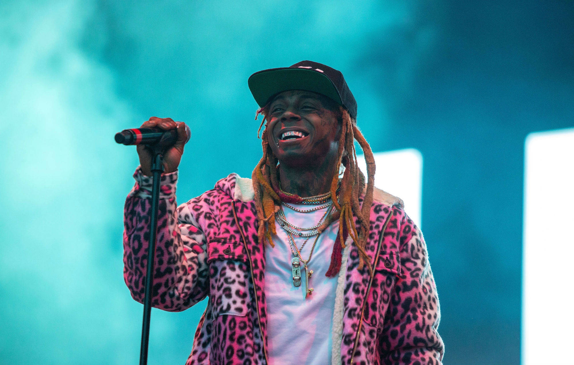 Lil Wayne 桌布 壁紙 — 一位面帶微笑、梳著辮子的饒舌歌手在藍色舞台燈光下穿著粉紅色豹紋外套表演。