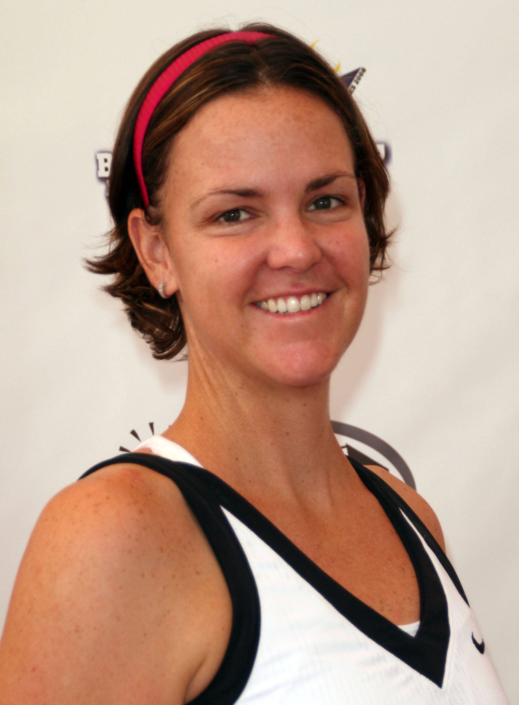 Tennis 桌布 壁紙 — 一位面帶微笑、留著短棕髮、戴著粉紅色頭帶的女性，在純白色背景前穿著白色和黑色的運動上衣。