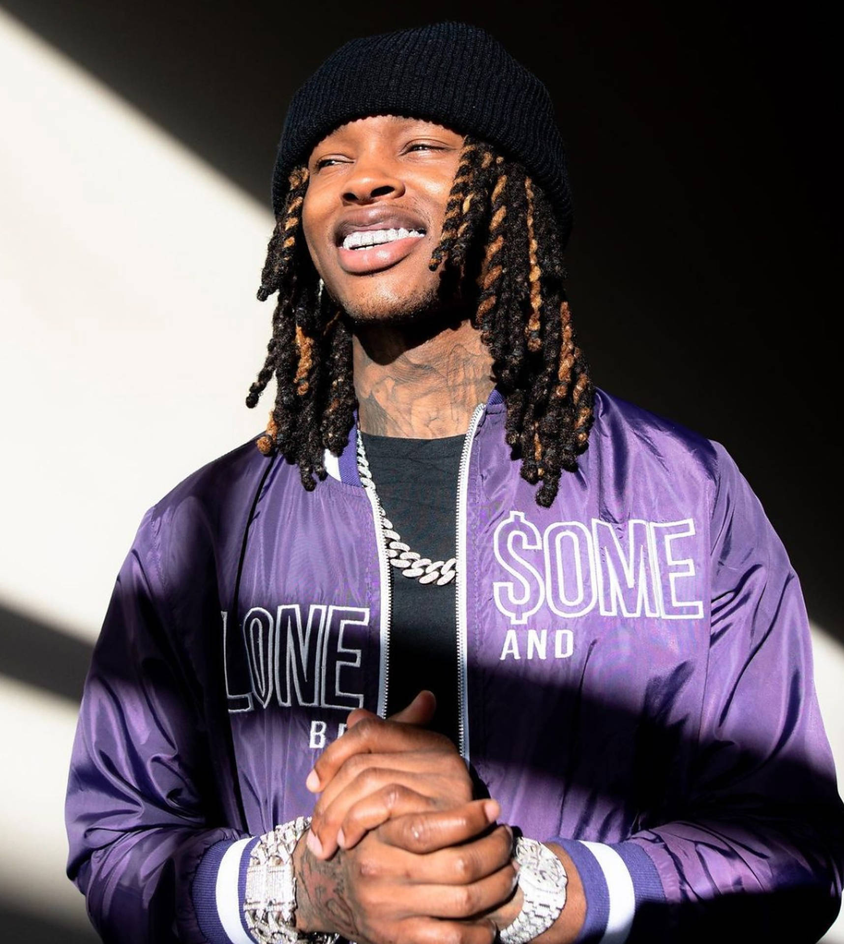 留著辮子的男士，身穿紫色外套和黑色毛帽，雙手合十微笑。 — King Von 壁紙