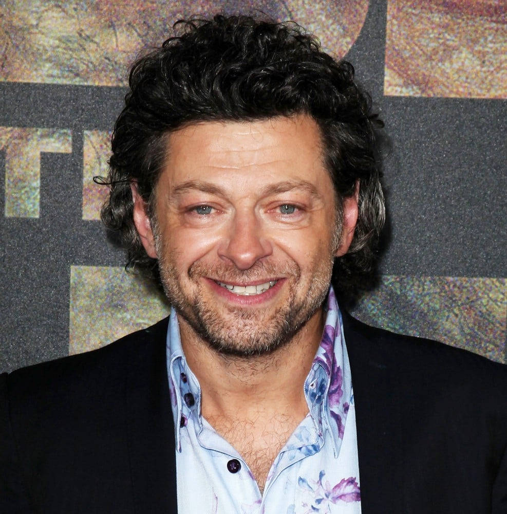 actor 桌布 壁紙 — 一位面帶微笑、留著黑色捲髮和鬍鬚的男子，在紋理背景前穿著黑色西裝外套，內搭花卉圖案襯衫。