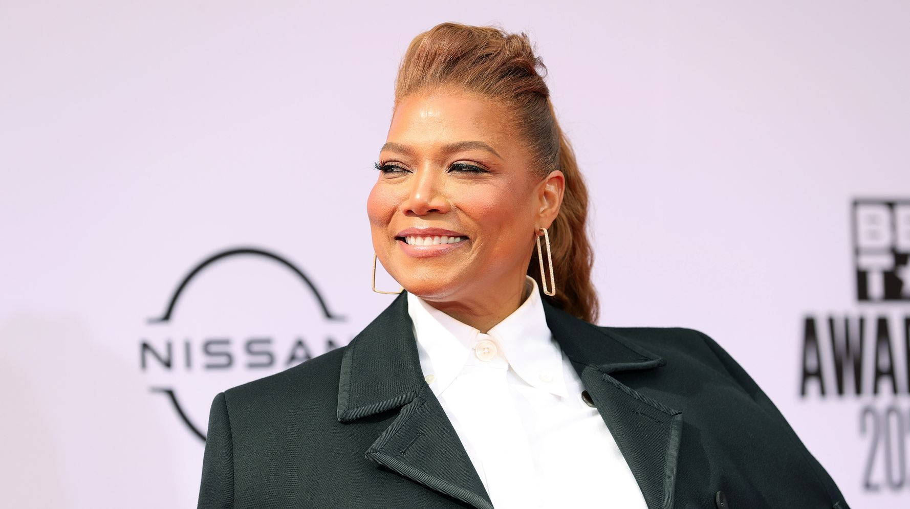  壁紙 — 一位面帶微笑、頭髮造型、戴著金色耳環的女性，在BET Awards紅地毯上穿著黑色西裝外套擺姿勢。