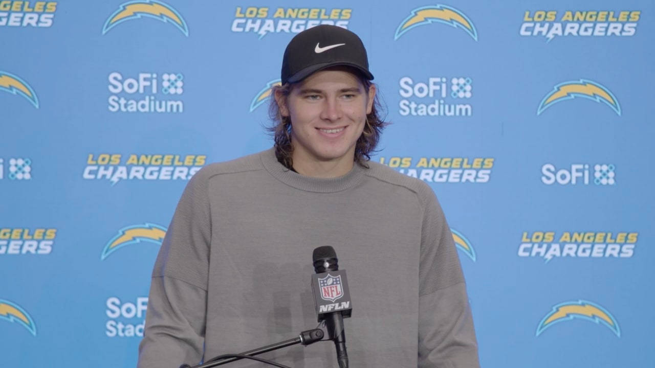 Herbert 桌布 壁紙 — 一位面帶微笑的NFL球員，戴著黑色帽子，穿著灰色運動衫，站在麥克風前，背景是藍色的洛杉磯電光隊。