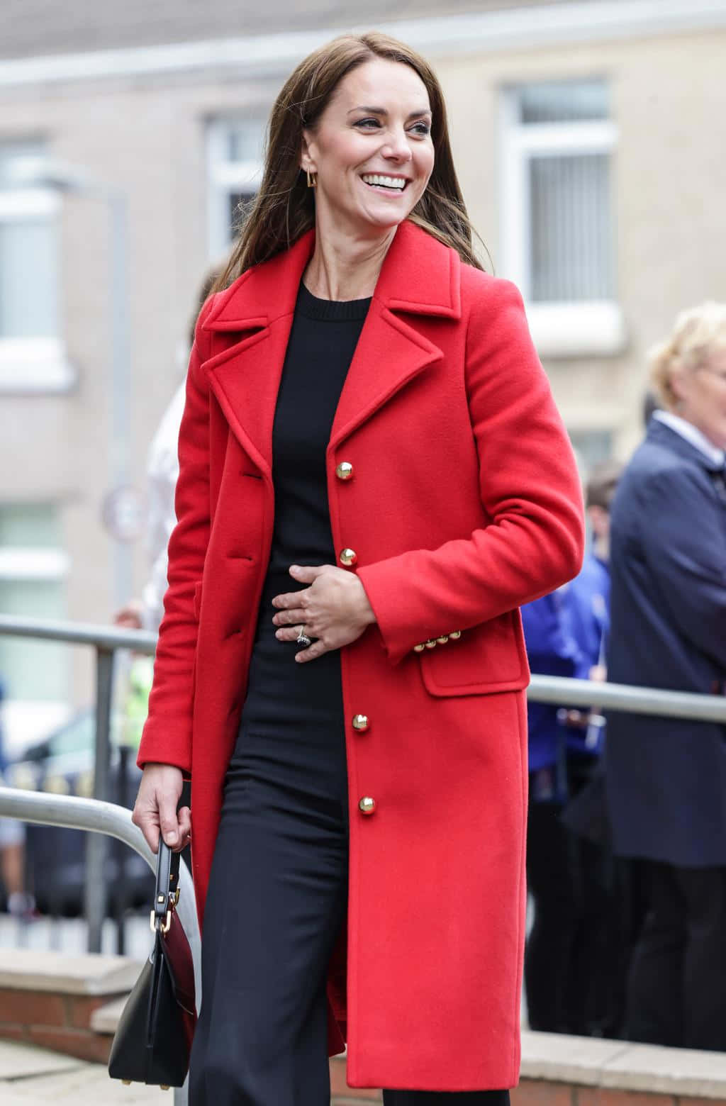 Red Coat 桌布 壁紙 — 一位面帶微笑的女性，身穿鮮紅色外套和黑色服裝，帶著愉悅的表情在戶外行走。