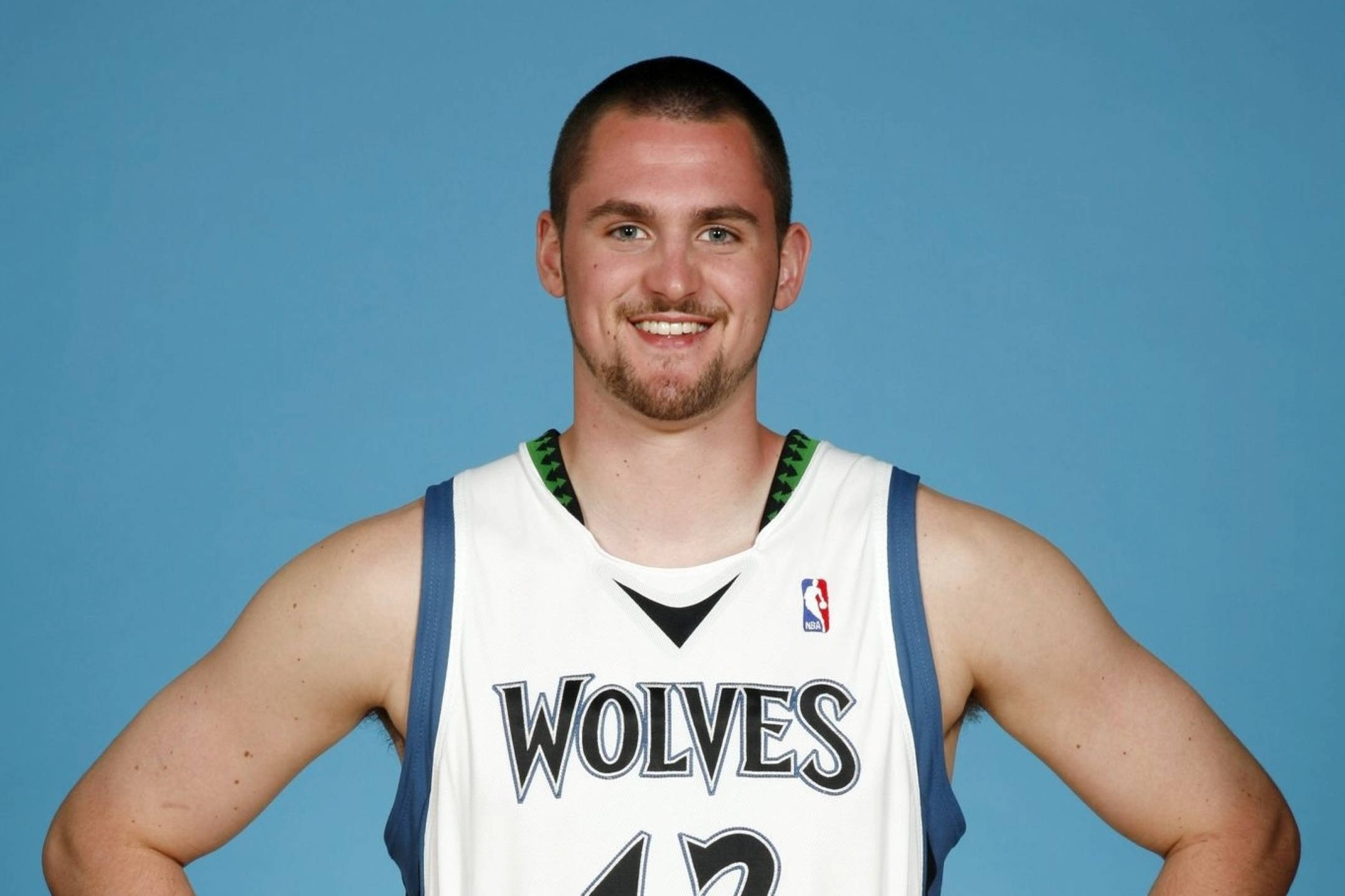 Kevin Love 桌布 壁紙 — 一位面帶微笑的籃球運動員身穿白色狼隊球衣，自信地站在純藍色攝影棚背景前。
