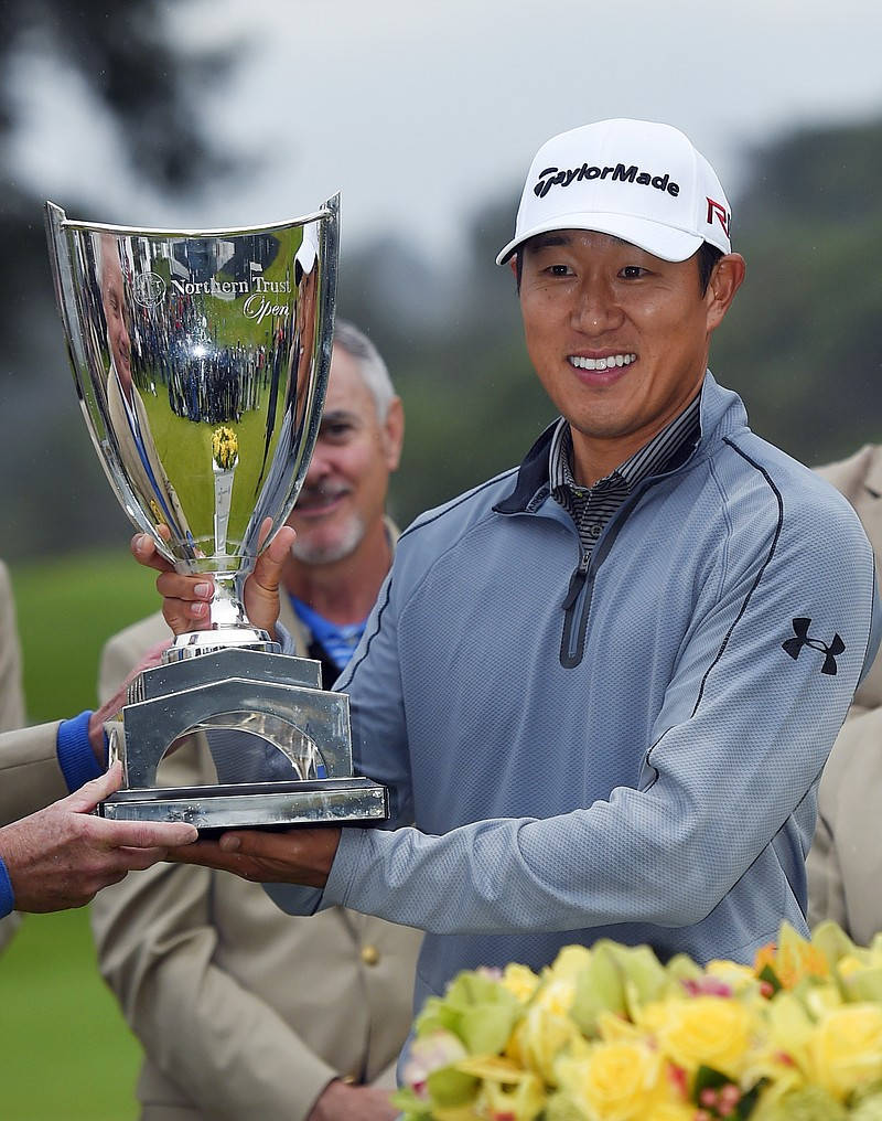 Trophy 桌布 壁紙 — 一位面帶微笑的高爾夫球手，身穿灰色套頭衫和白色帽子，在戶外自豪地高舉著一個大型銀色Northern Trust Open獎盃。