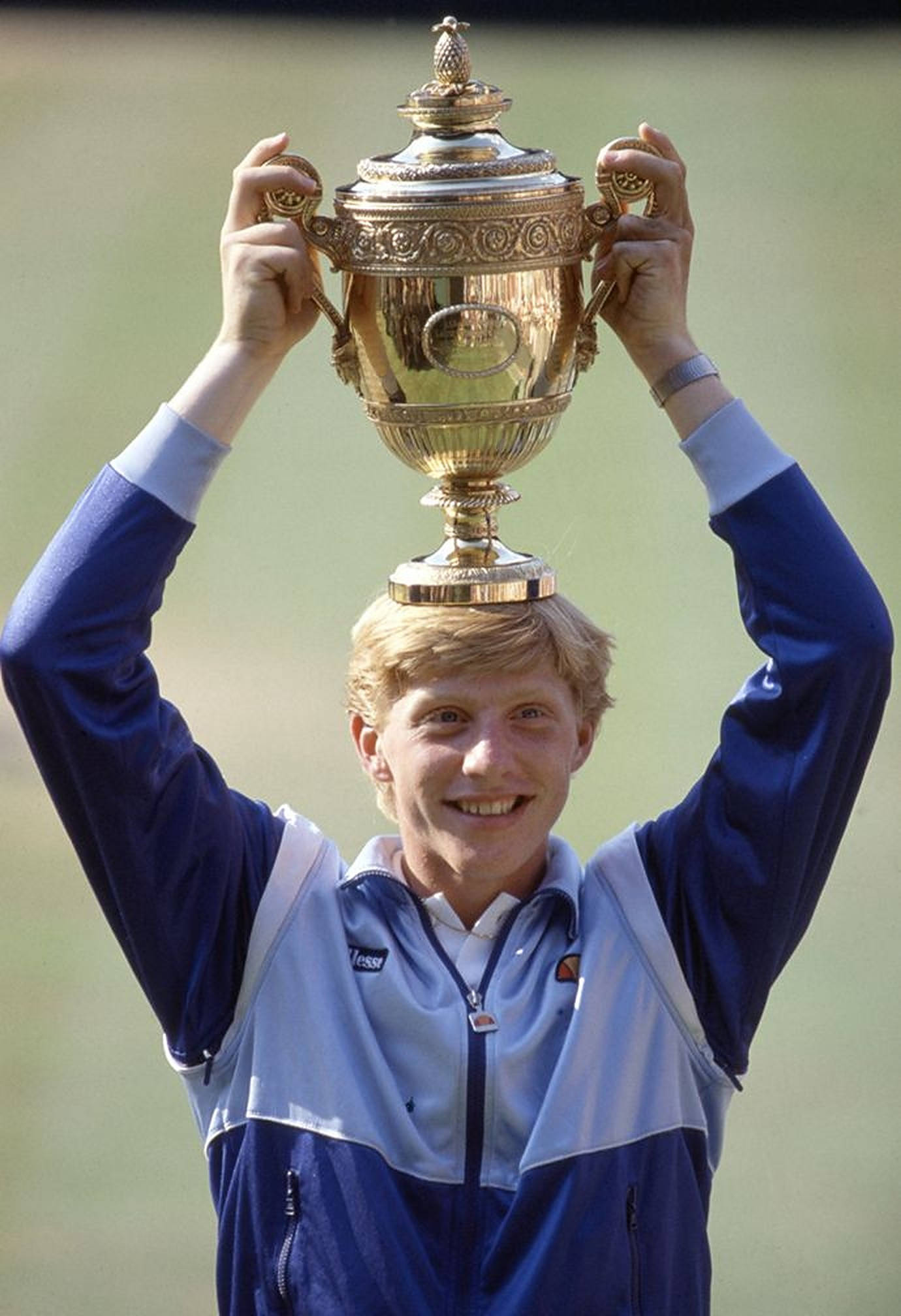 Boris Becker 桌布 壁紙 — 一位面帶微笑的高爾夫球手身穿藍白夾克，勝利地將一個華麗的大型金色獎盃高舉過頭頂。