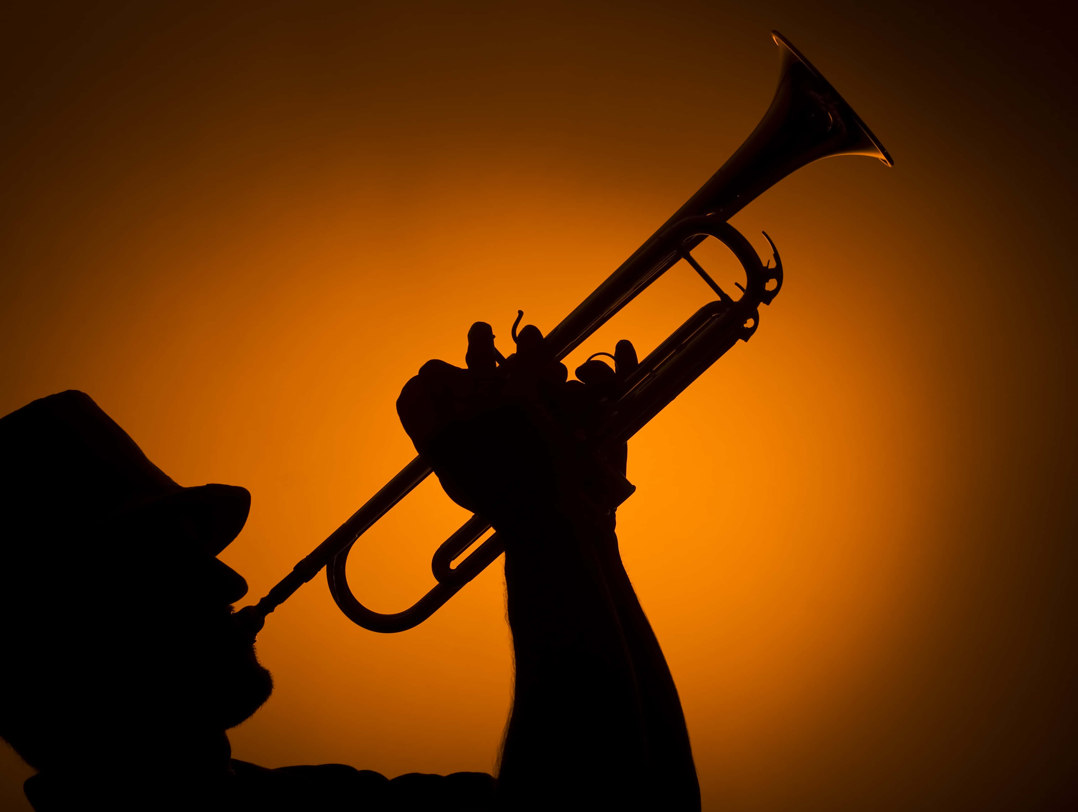 Jazz 桌布 壁紙 — 一位音樂家在溫暖發光的橙色背景下吹奏小號的剪影。