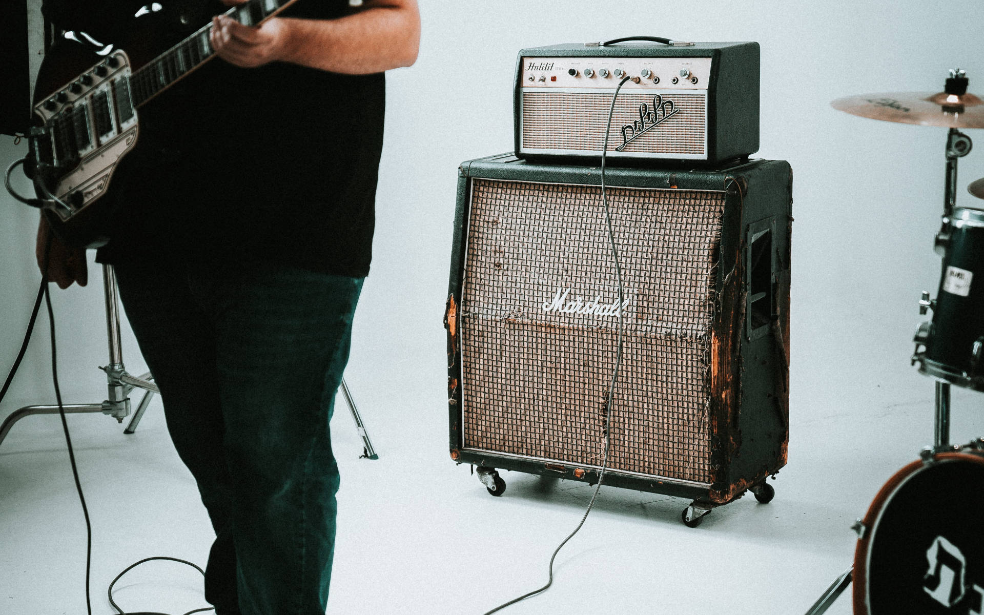 Marshall 桌布 壁紙 — 一位音樂家在簡約的工作室環境中，在復古的Marshall擴音器和鼓組旁邊彈奏吉他。