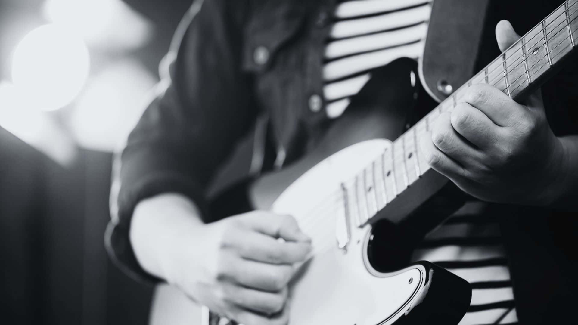 Black And White Guitar 桌布 壁紙 — 一位音樂家的雙手在明亮的舞台燈光下，以黑白風格熟練地彈奏白色電吉他。