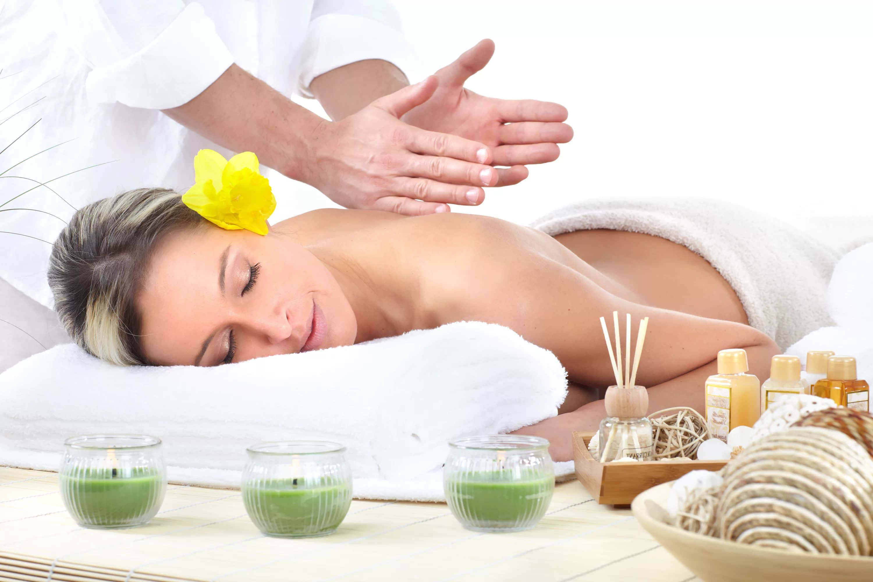 Massage 桌布 壁紙 — 一位頭上戴著黃花的寧靜女性，在綠色蠟燭和水療必需品的環繞下享受放鬆按摩。