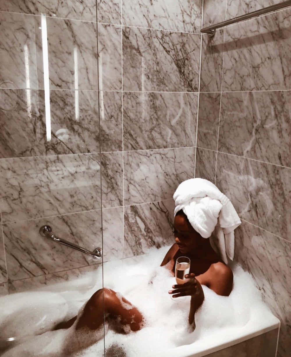 Boujee Aesthetic 桌布 壁紙 — 一位頭上裹著毛巾的女性在大理石瓷磚浴室中享受泡泡浴，手持一杯香檳放鬆身心。