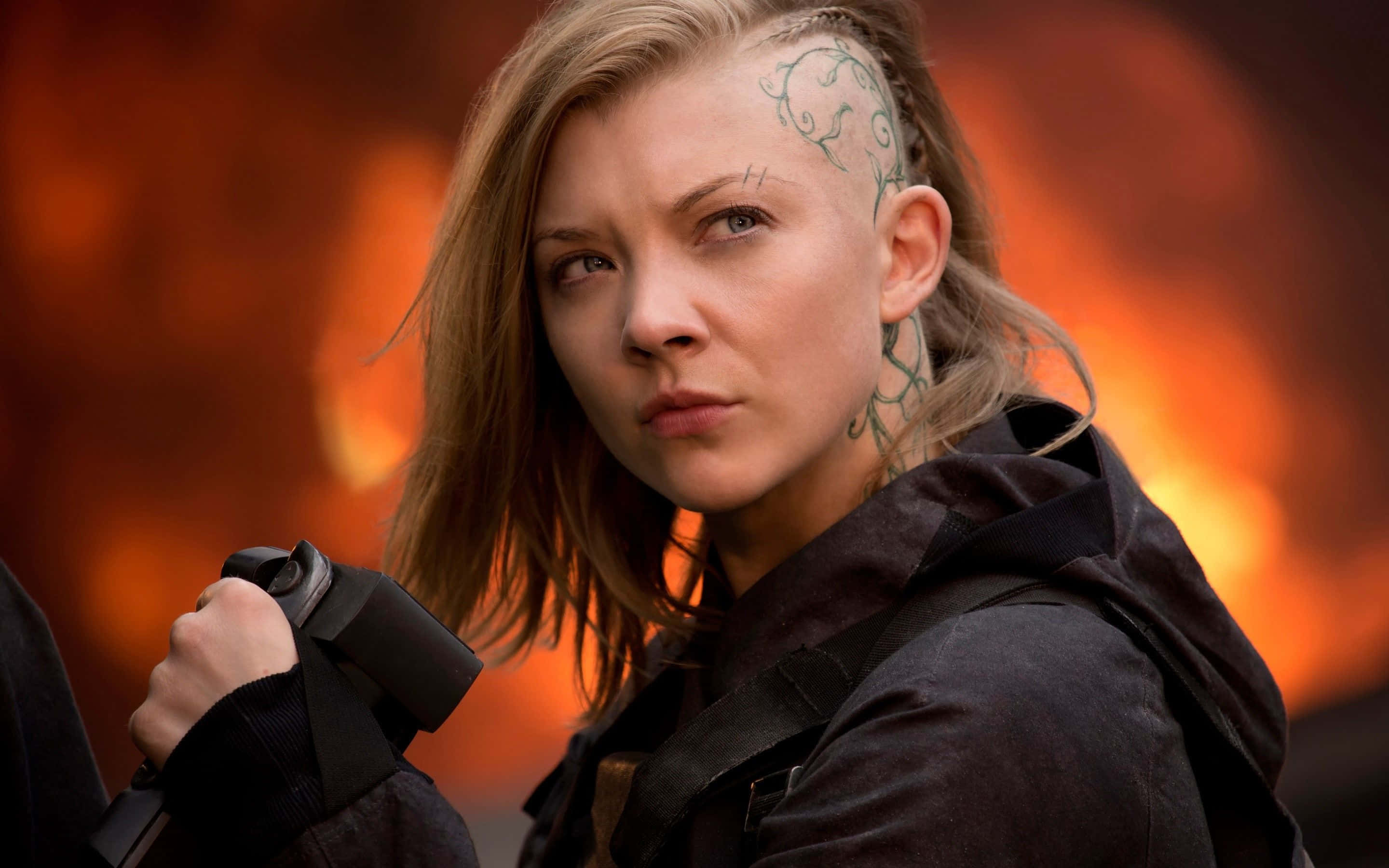 natalie dormer 桌布 壁紙 — 一位頭皮和脖子上有綠色藤蔓紋身的堅定女性，在熾熱的橙色背景下手持武器。