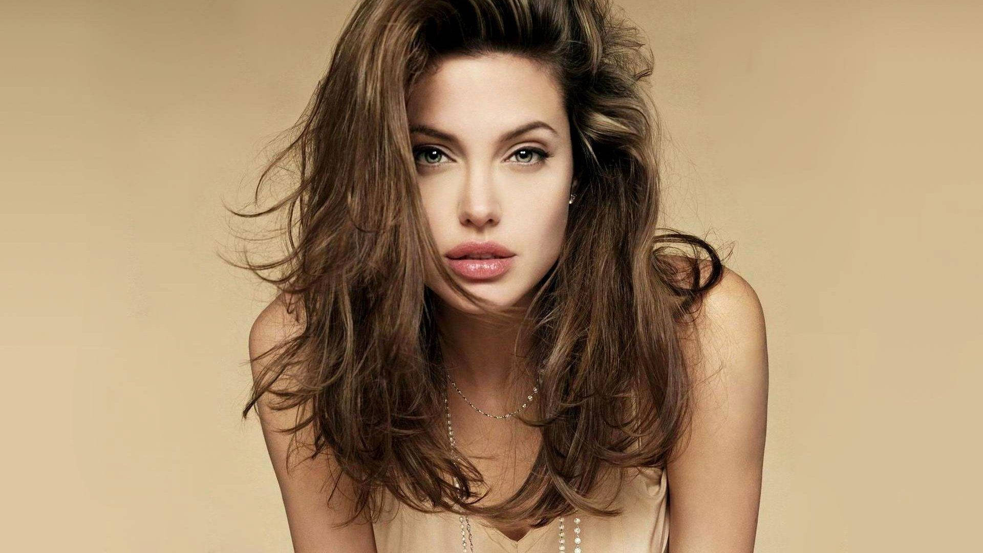 Angelina 桌布 壁紙 — 一位頭髮凌亂的棕色頭髮、擁有引人注目的綠色眼睛的女性，在柔和的米色背景下直視鏡頭。