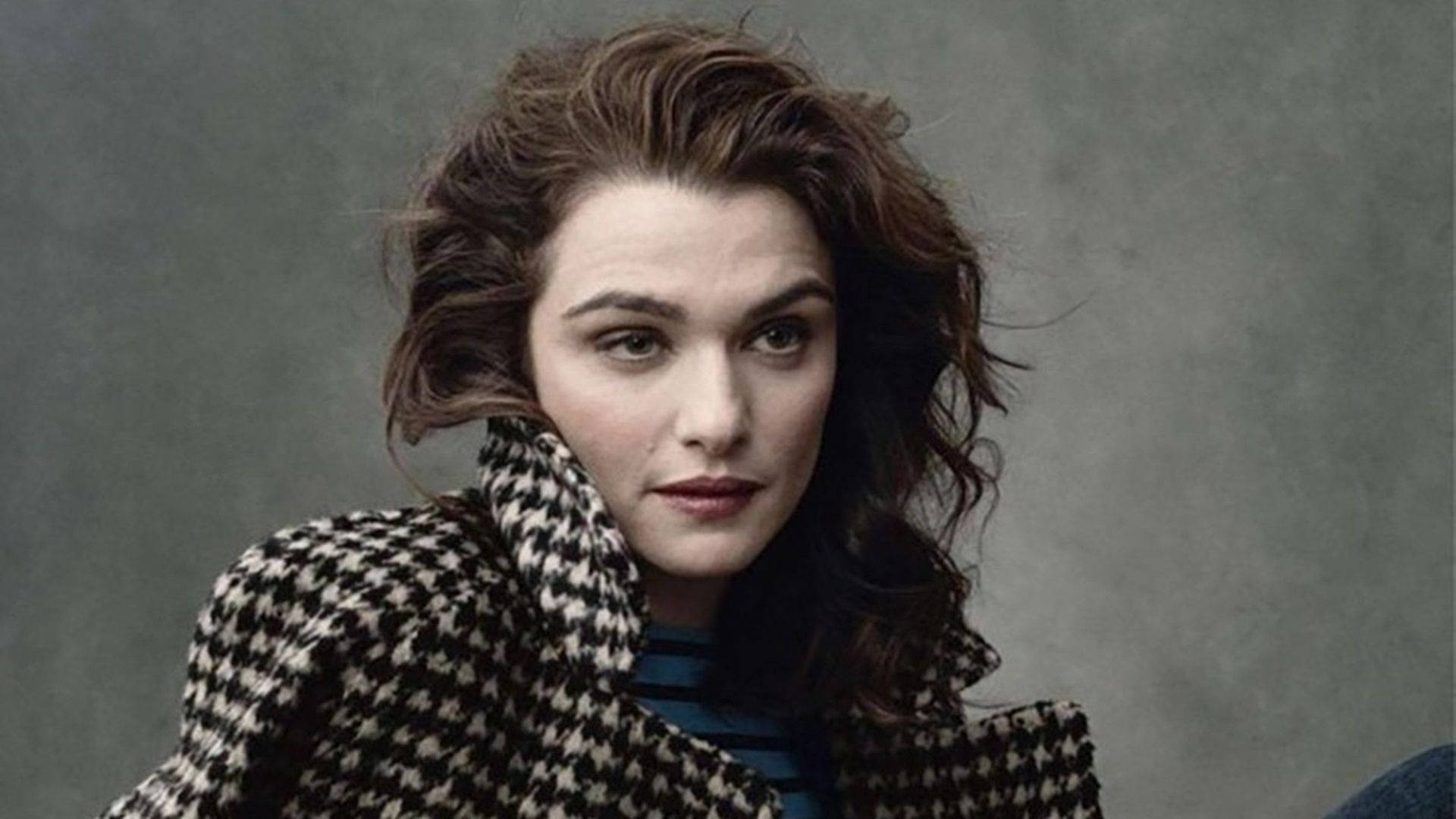 Rachel Weisz 桌布 壁紙 — 一位頭髮凌亂的棕色頭髮女性，在柔和的灰色背景下穿著黑白千鳥格大衣。