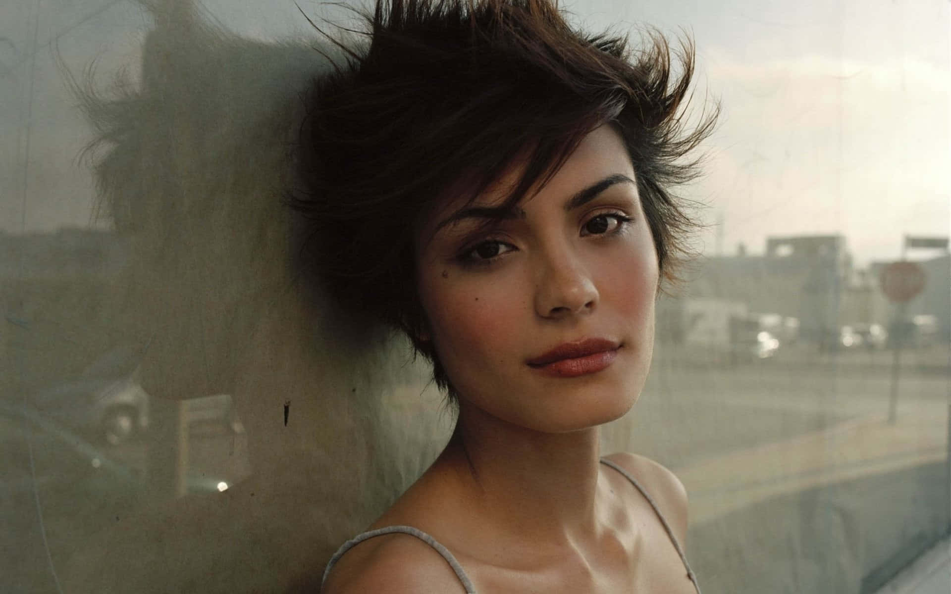 Shannyn Sossamon 桌布 壁紙 — 一位頭髮凌亂的深色頭髮女性靠在一扇霧氣朦朧的窗戶上，俯瞰著模糊的城市街道。