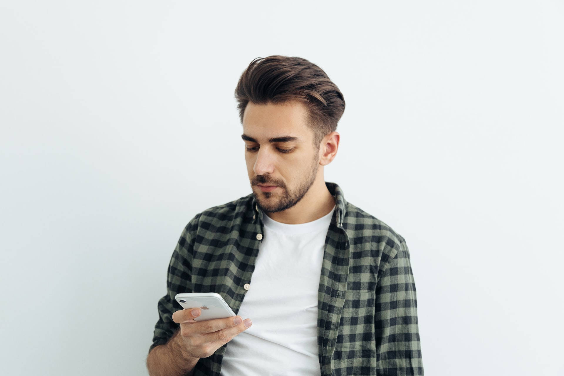 Haircut 桌布 壁紙 — 一位頭髮和鬍子經過造型的男士，穿著格紋襯衫，在純白背景前專注地看著他的智慧型手機。