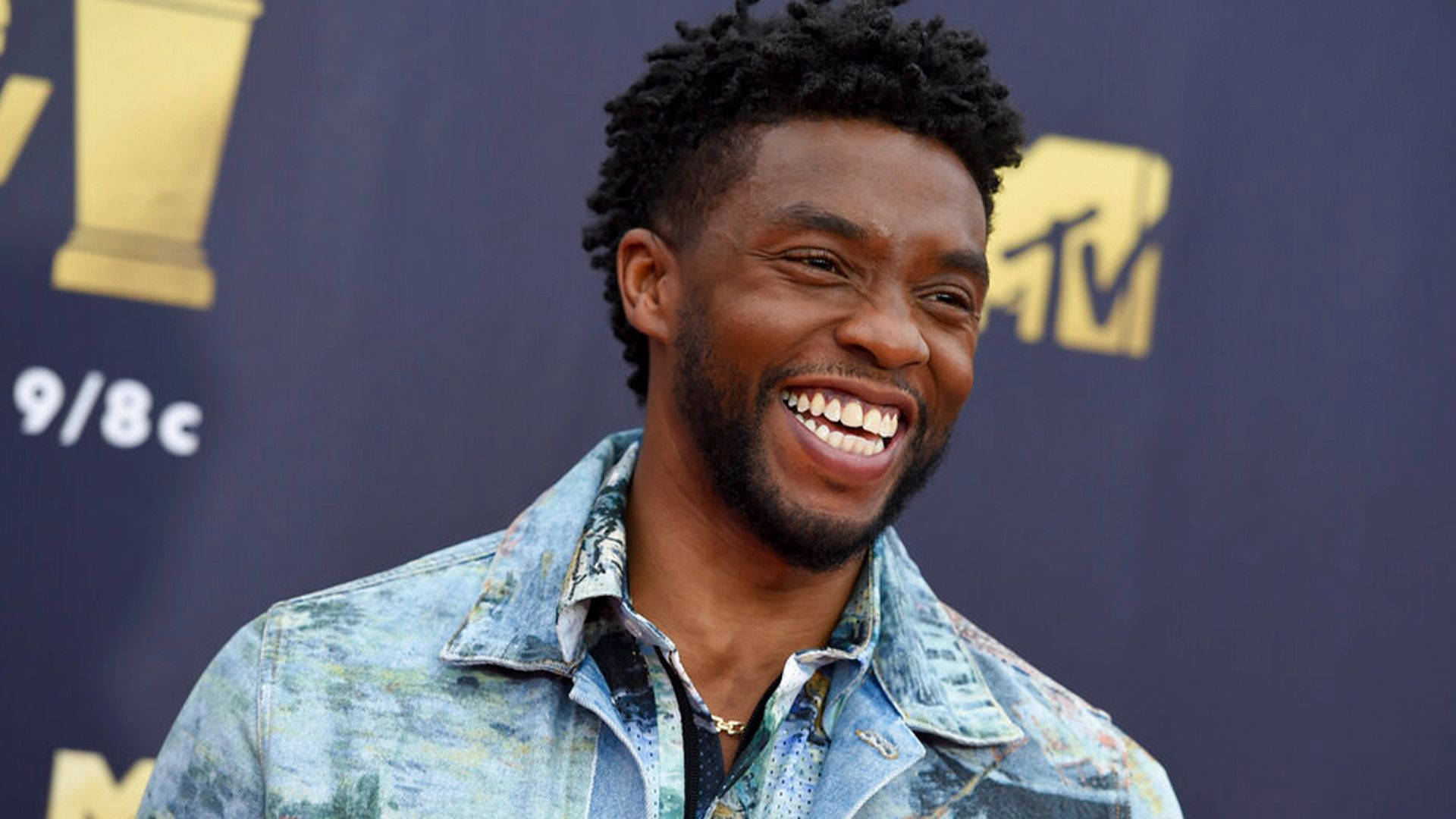 Chadwick 桌布 壁紙 — 一位頭髮捲曲的快樂男子，穿著圖案牛仔外套，在深藍色MTV背景下露出燦爛笑容。
