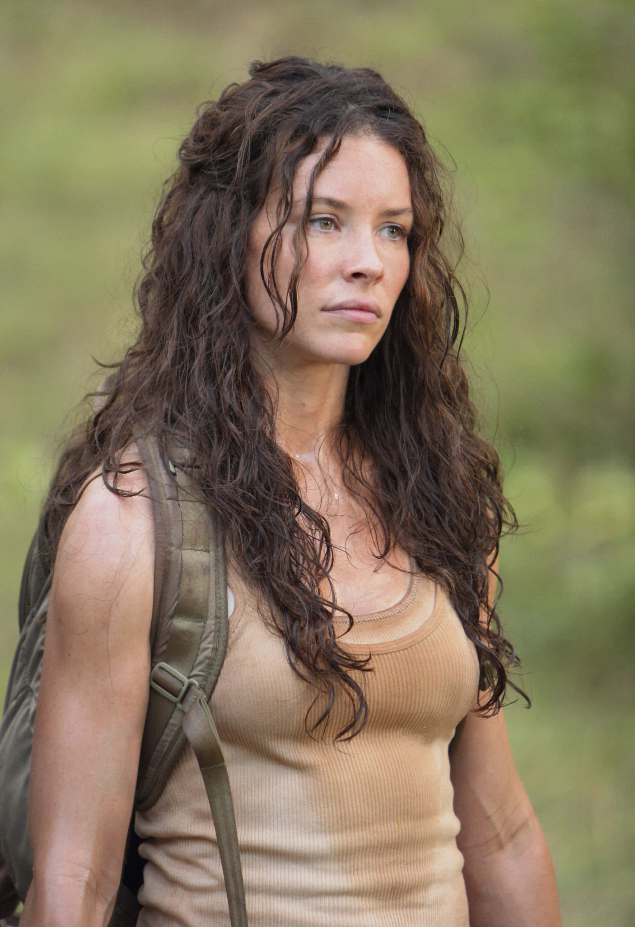 evangeline lilly 桌布 壁紙 — 一位頭髮濕漉漉、捲曲、背著背包的女性站在模糊的綠色田野中，眺望遠方。