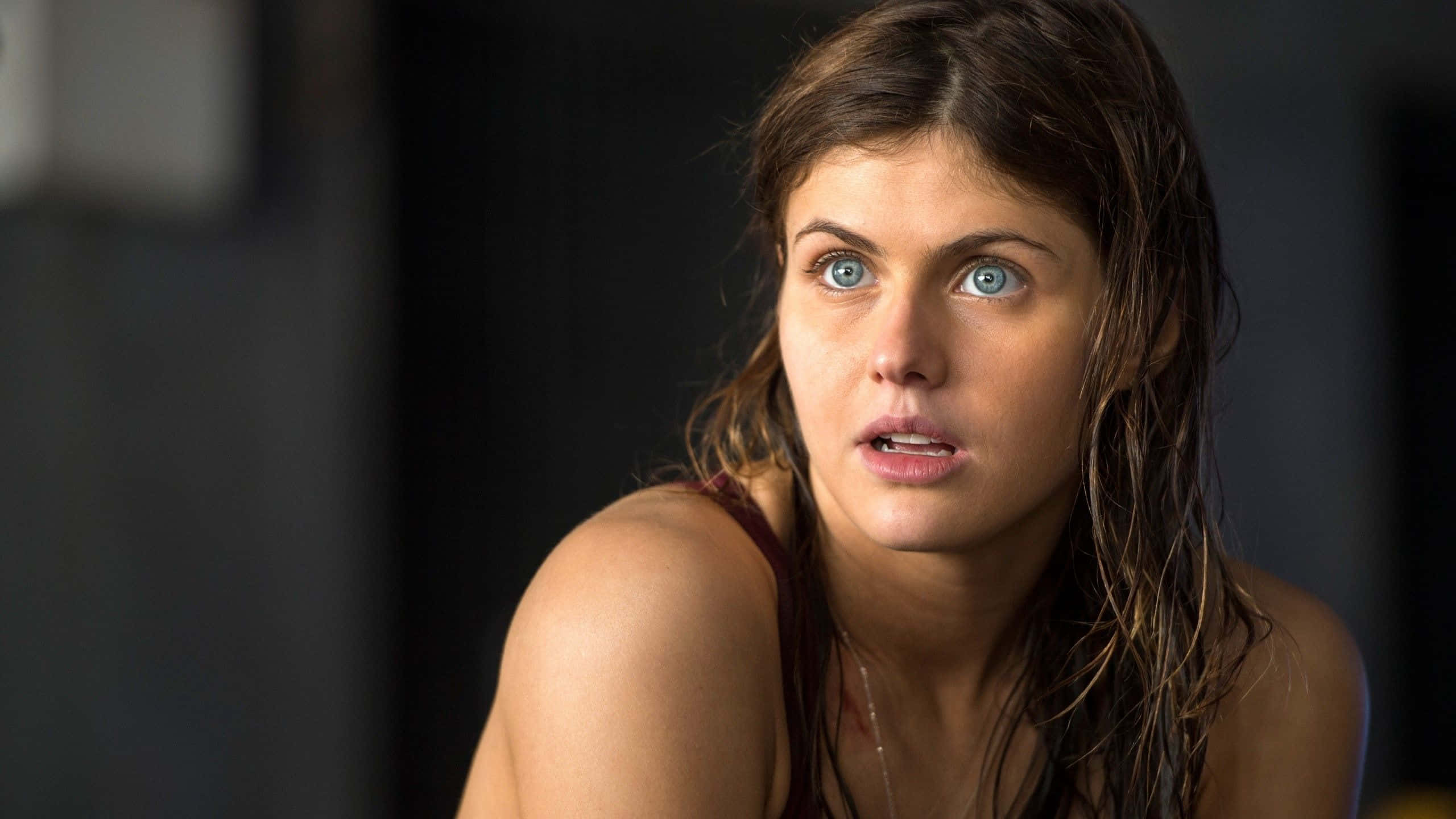 Alexandra Daddario 桌布 壁紙 — 一位頭髮濕透、擁有強烈藍色眼睛的女性，在黑暗模糊的背景前震驚地凝視。