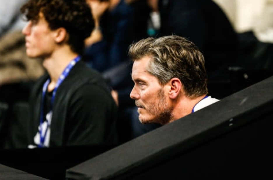 Tennis 桌布 壁紙 — 一位頭髮灰白、留著鬍鬚的男子專注地坐在體育場座位上，注視著前方的事件。