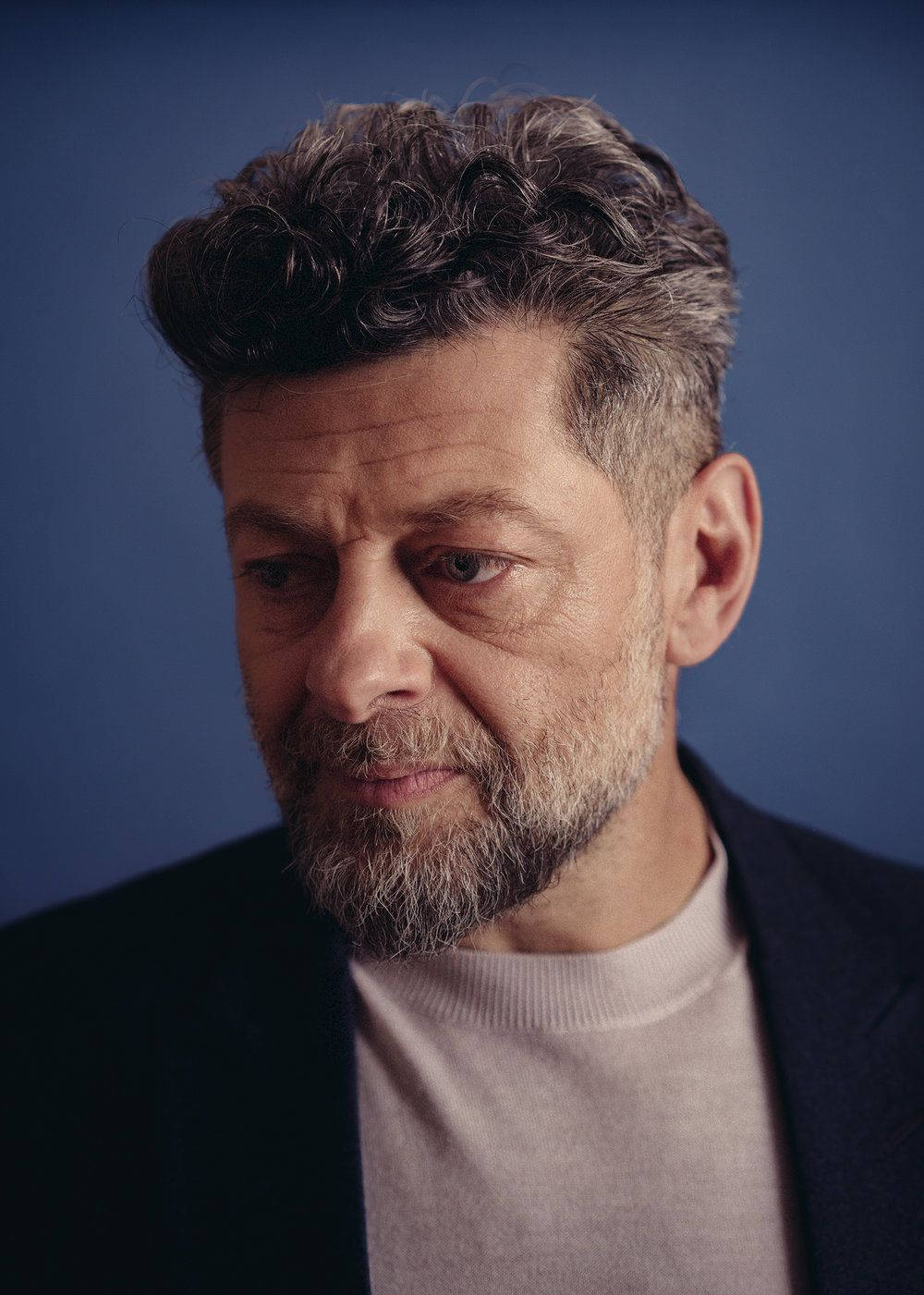 actor 桌布 壁紙 — 一位頭髮灰白捲曲、留鬍子的男士，在純藍色攝影棚背景前若有所思地凝視。