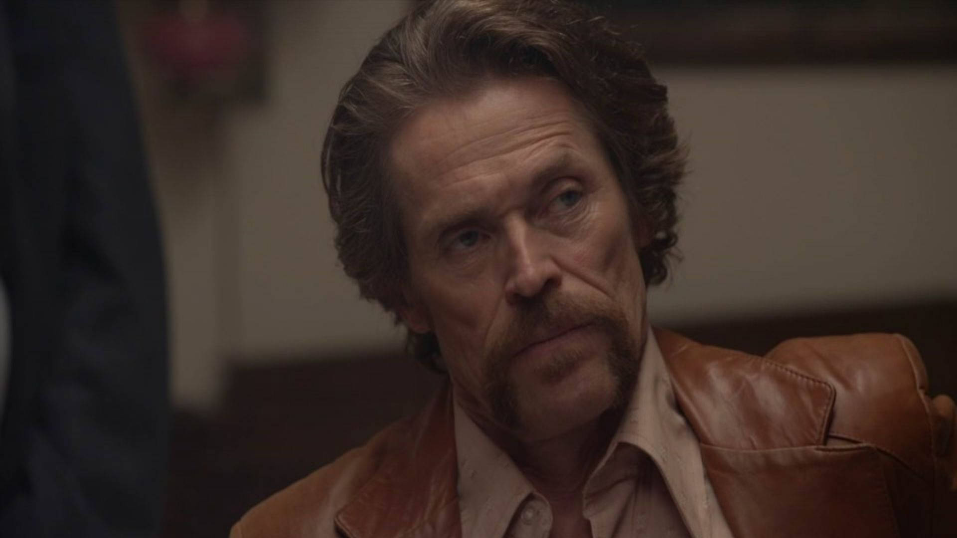 Willem Dafoe 桌布 壁紙 — 一位頭髮花白、留鬍子的男士在昏暗的房間裡穿著棕色皮夾克。
