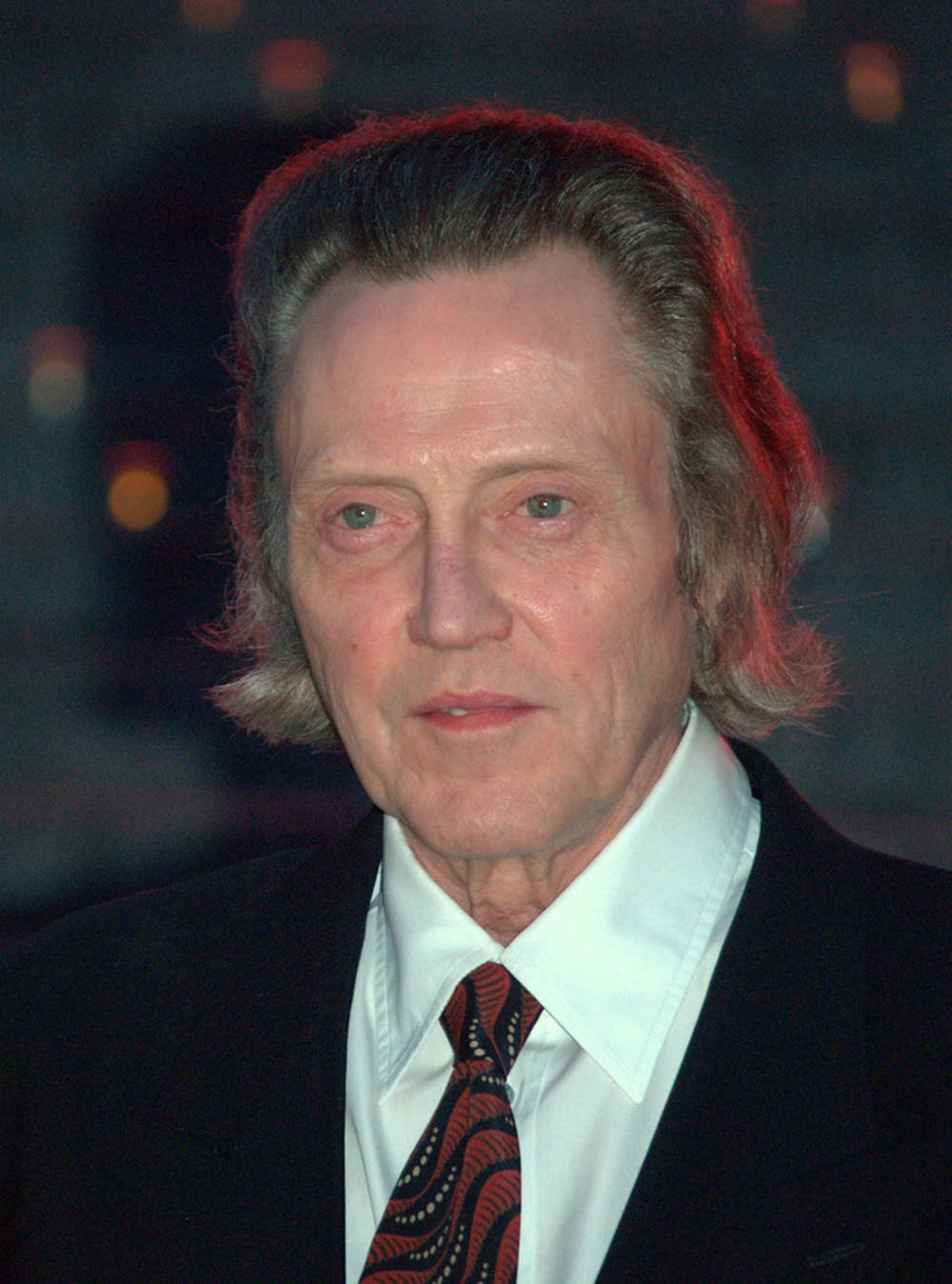 Celebrity 桌布 壁紙 — 一位頭髮花白、眼神銳利的男士特寫肖像，身穿深色西裝和圖案領帶，背景模糊帶有溫暖的散景燈光。