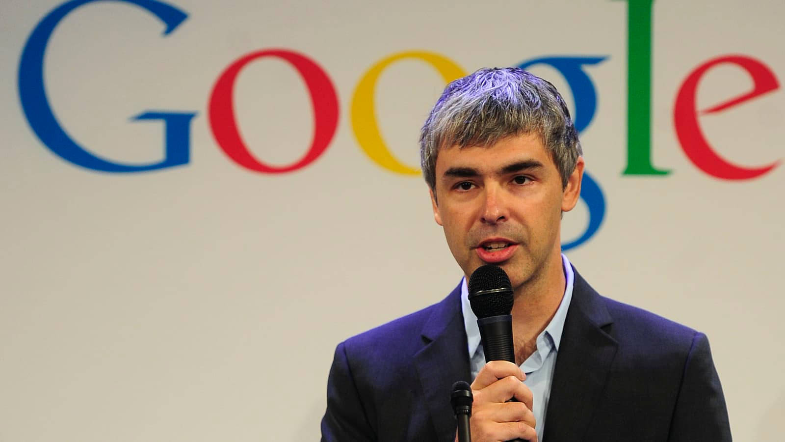 google 桌布 壁紙 — 一位頭髮花白的男士在色彩繽紛的Google標誌背景前對著麥克風講話。