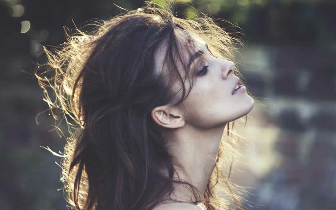 Side Profile 桌布 壁紙 — 一位頭髮蓬鬆深色的女子向後仰頭，金色陽光在模糊的戶外背景下凸顯髮絲。