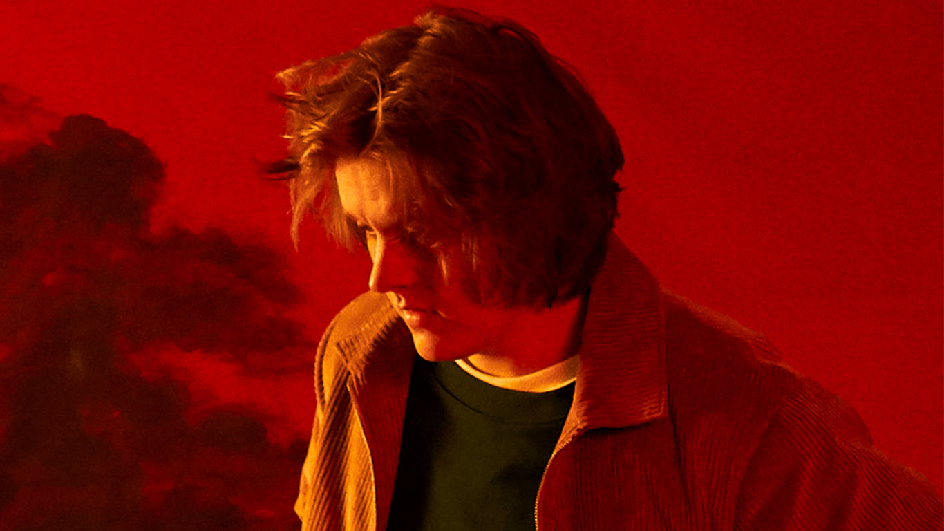 Lewis Capaldi 桌布 壁紙 — 一位頭髮蓬鬆的年輕男子在帶有煙霧陰影的鮮紅色背景下向下凝視。