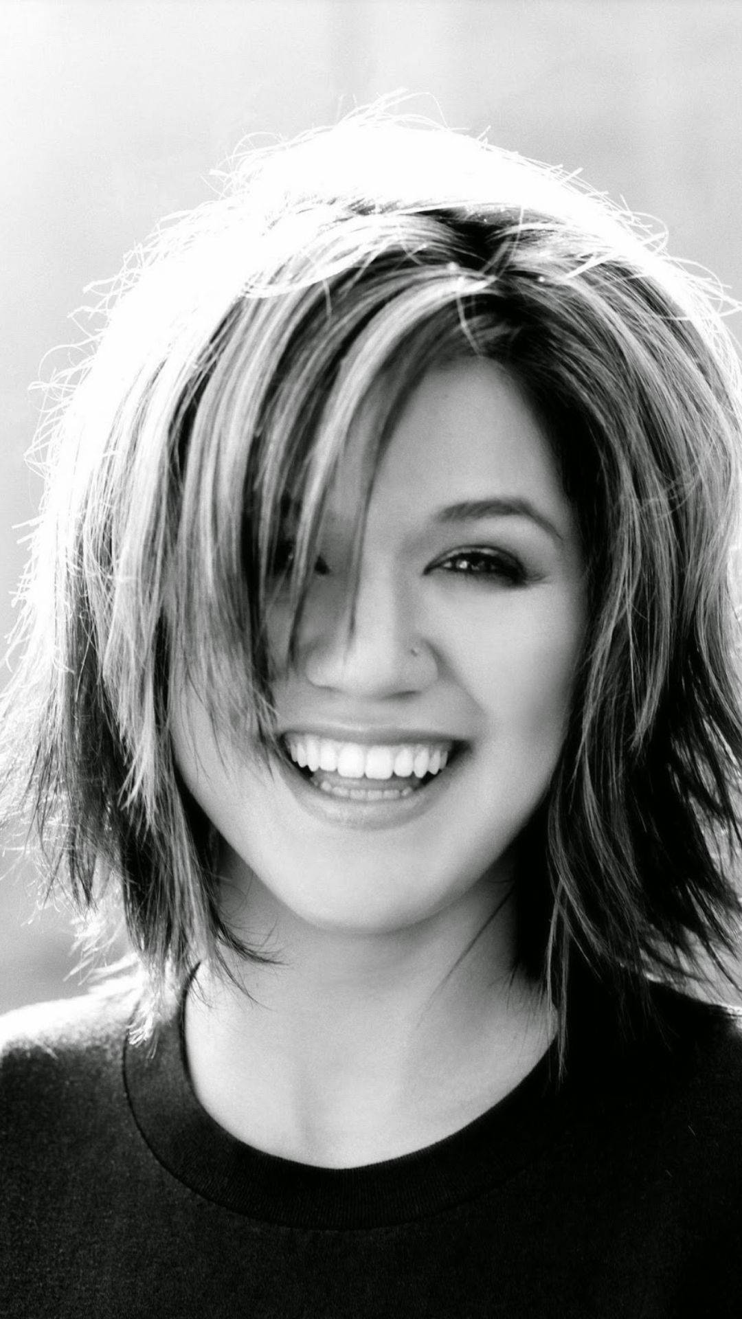 Kelly Clarkson 桌布 壁紙 — 一位頭髮蓬鬆的快樂女性在高對比度的黑白肖像中燦爛地閃耀。