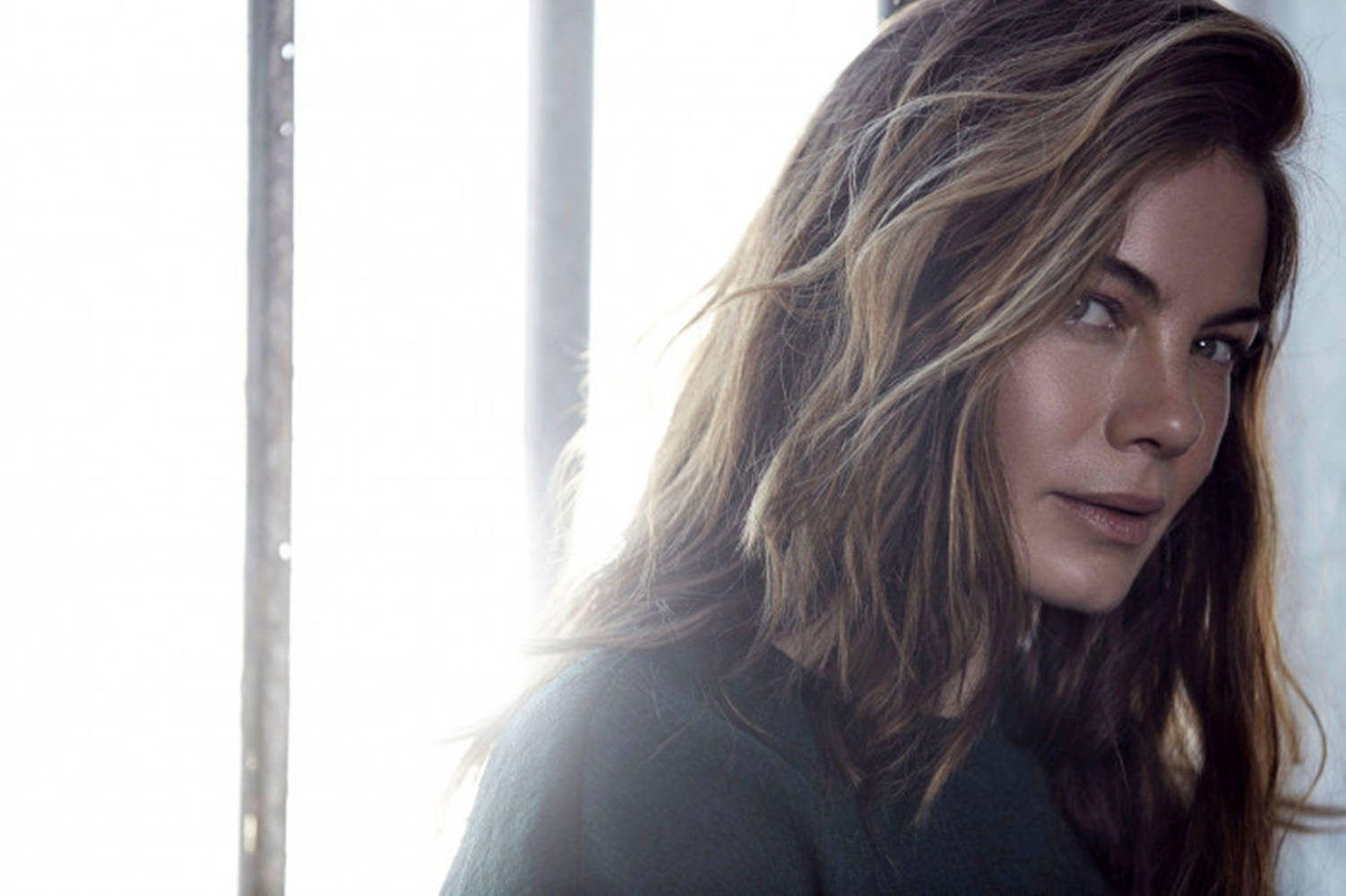 Michelle Monaghan 桌布 壁紙 — 一位頭髮蓬鬆的棕髮女性若有所思地凝視著鏡頭，被明亮的窗光柔和地照亮。