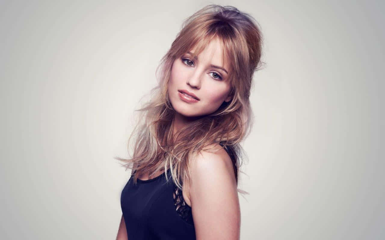 dianna agron 桌布 壁紙 — 一位頭髮蓬鬆的金髮女子穿著黑色上衣，在純淺灰色背景前柔和地凝視鏡頭。