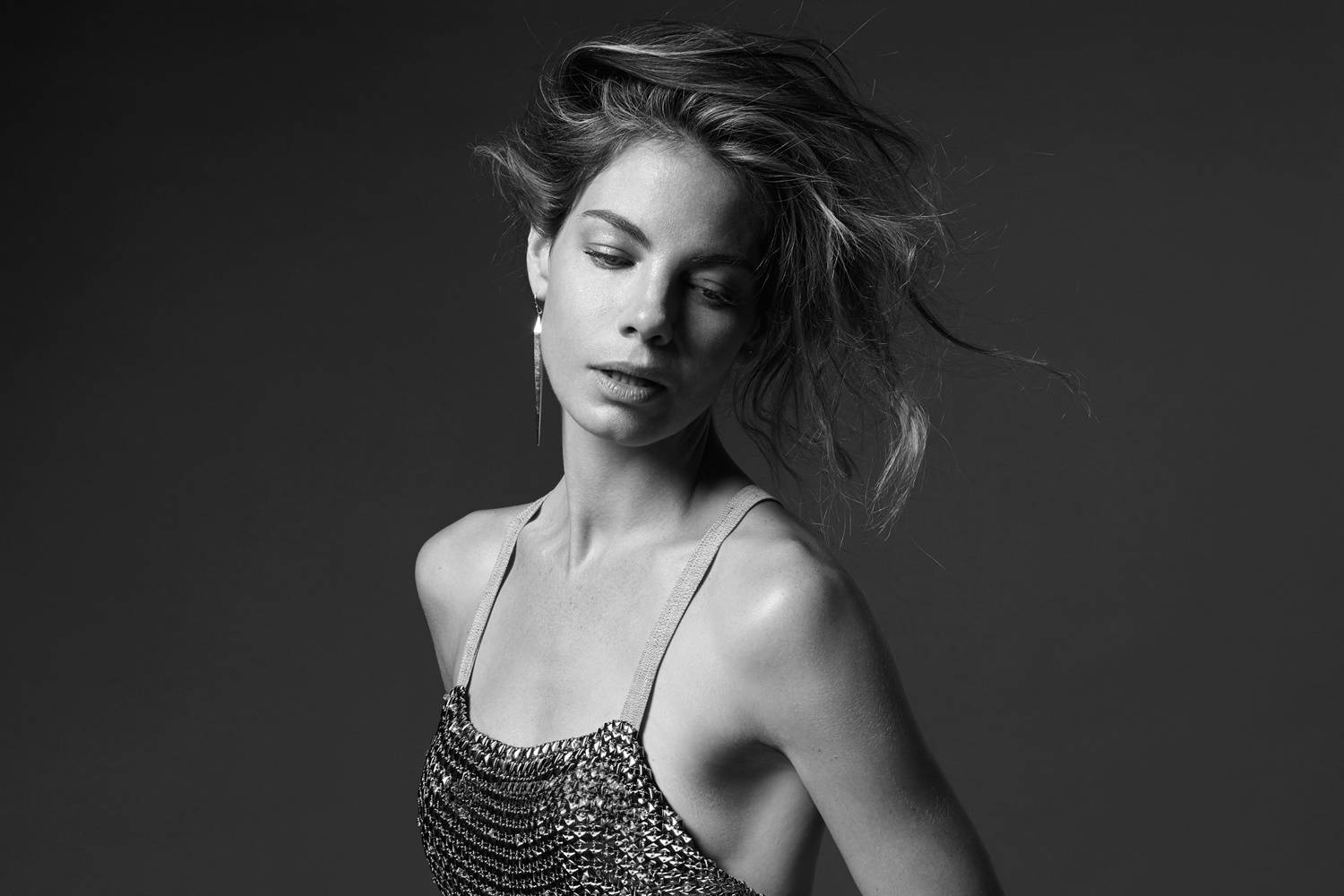 Michelle Monaghan 桌布 壁紙 — 一位頭髮被風吹亂、身穿鎖子甲上衣的女性，在一張充滿氣氛的黑白工作室肖像照中向下凝視。