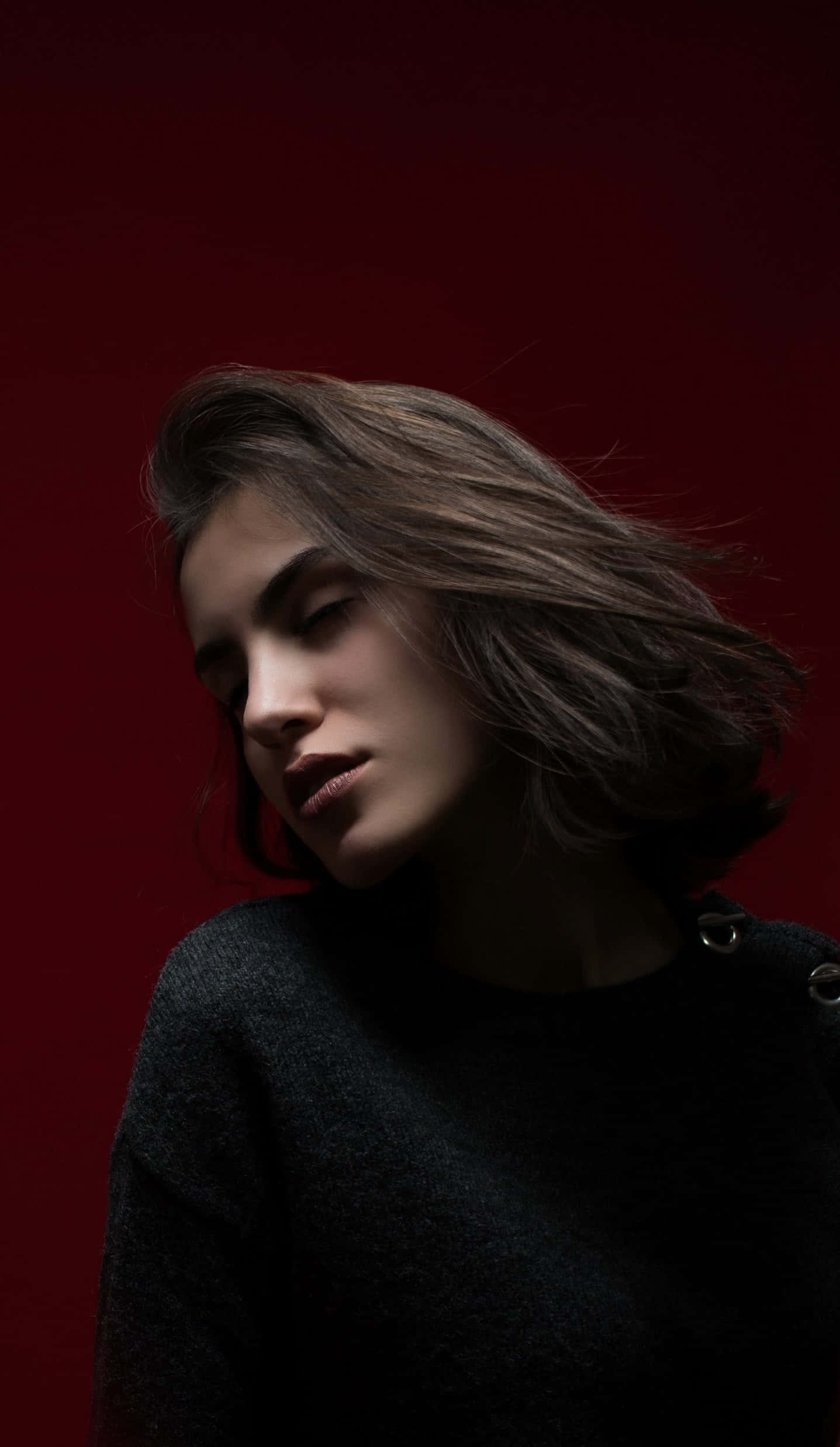 Woman Beautiful 桌布 壁紙 — 一位頭髮被風吹亂的女子在深紅色背景下，於戲劇性的攝影棚燈光中向下凝視。