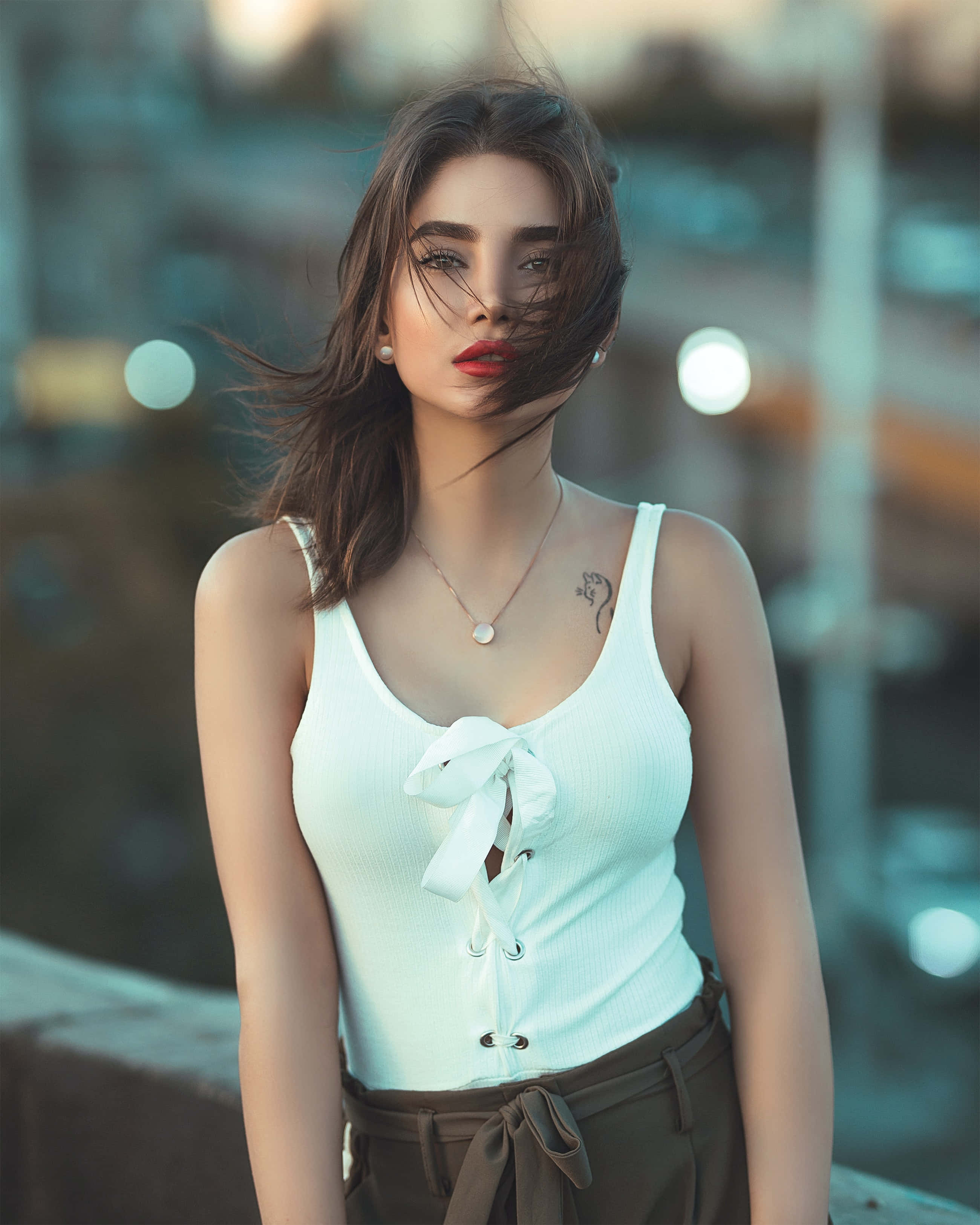 Beautiful Woman 桌布 壁紙 — 一位頭髮被風吹拂、紅唇的女性，在黃昏時分自信地穿著白色上衣，背景是模糊的城市天際線。