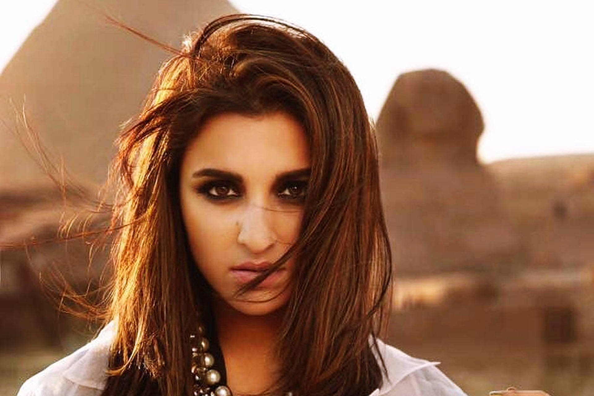 Parineeti 桌布 壁紙 — 一位頭髮被風吹拂的女性，在金色時刻以金字塔和獅身人面像為背景，凝視著。