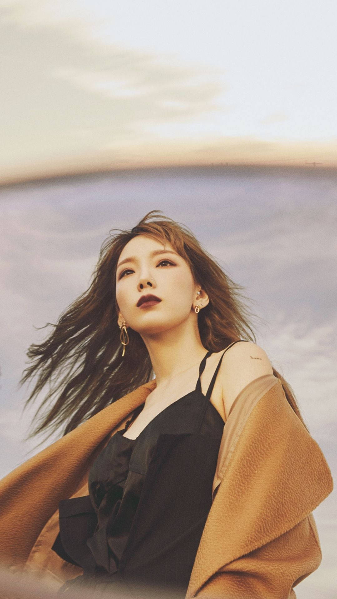 태연 桌布 壁紙 — 一位頭髮被風吹拂的女性，在黃金時刻仰望柔和粉彩色的天空。